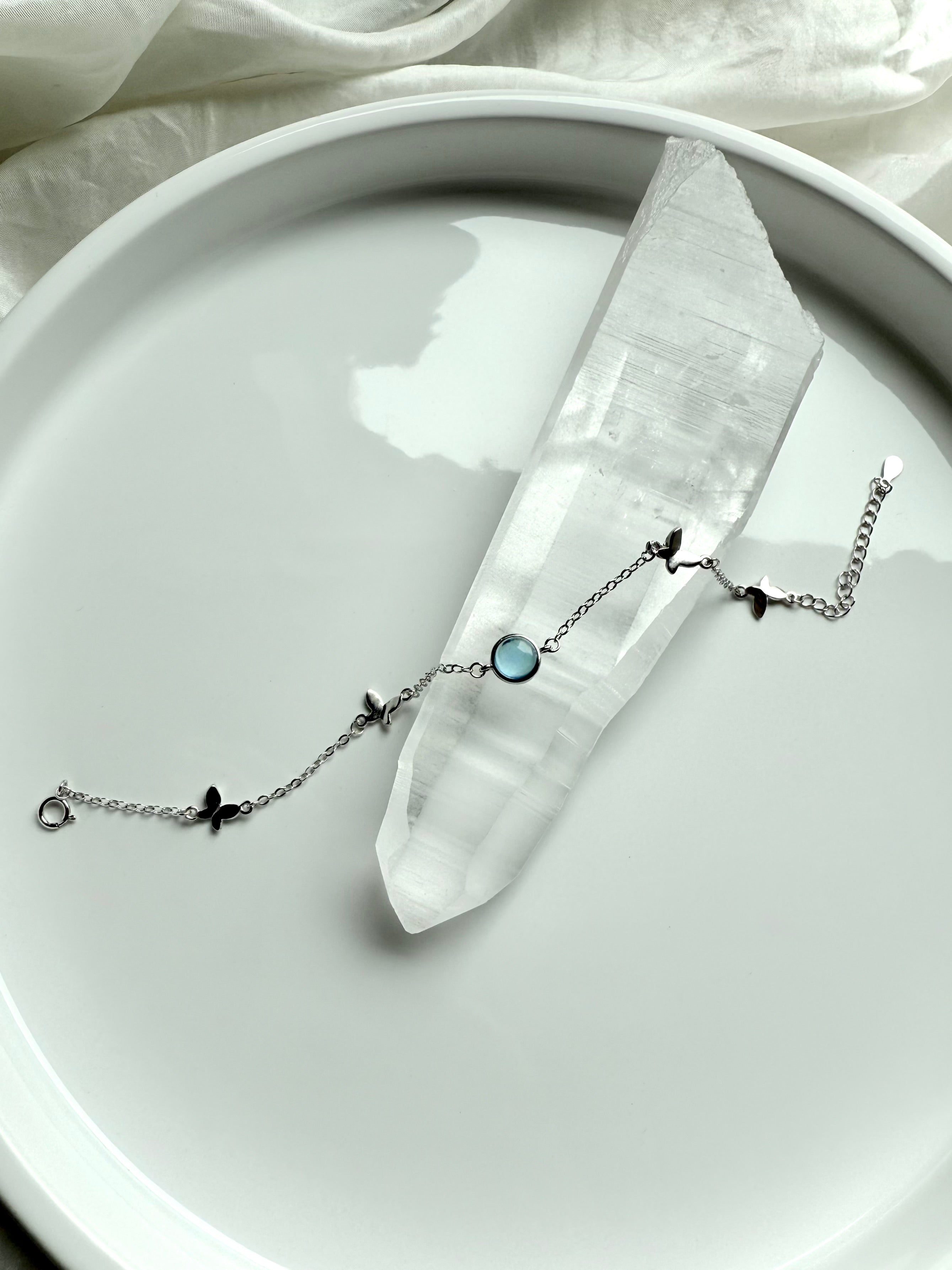 Aquamarine gemstone bracelet with silver butterfly charms displayed across a clear quartz point for spiritual healing and clarity