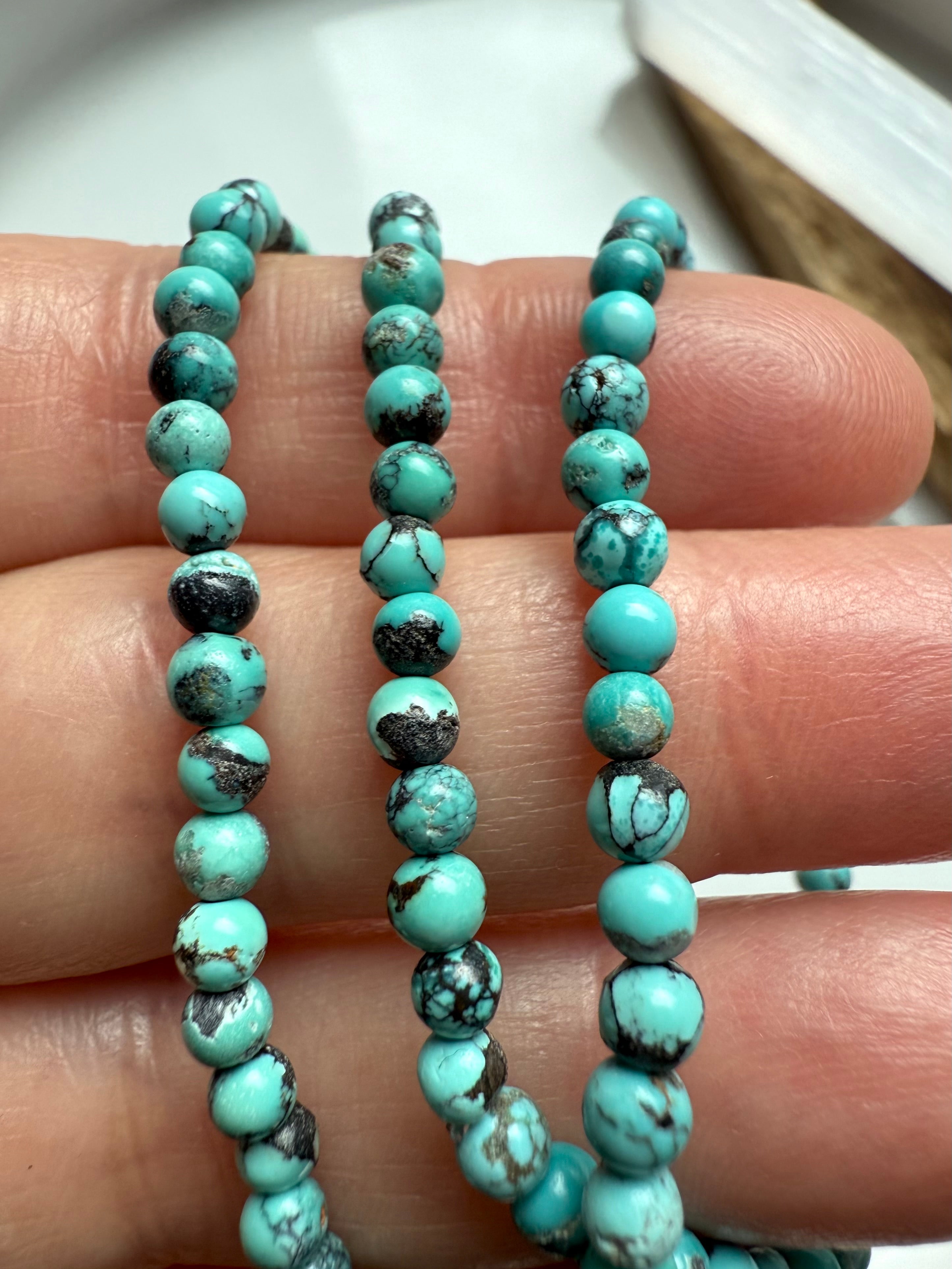 Close-up of small turquoise round beads with black matrix and natural color variation