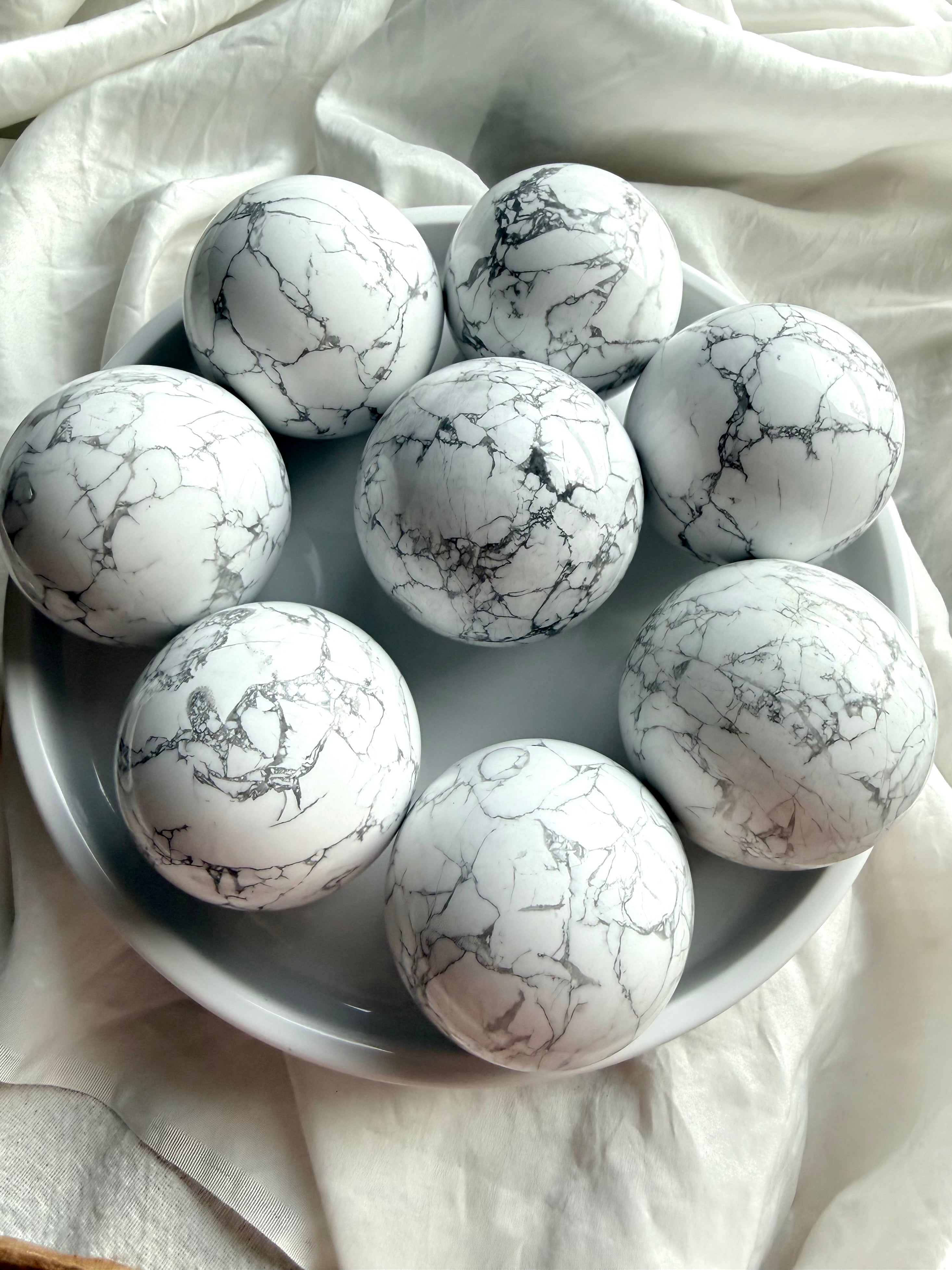 Assorted polished Howlite crystal spheres on white tray, natural white stone with gray veining for anxiety relief and serene altar décor