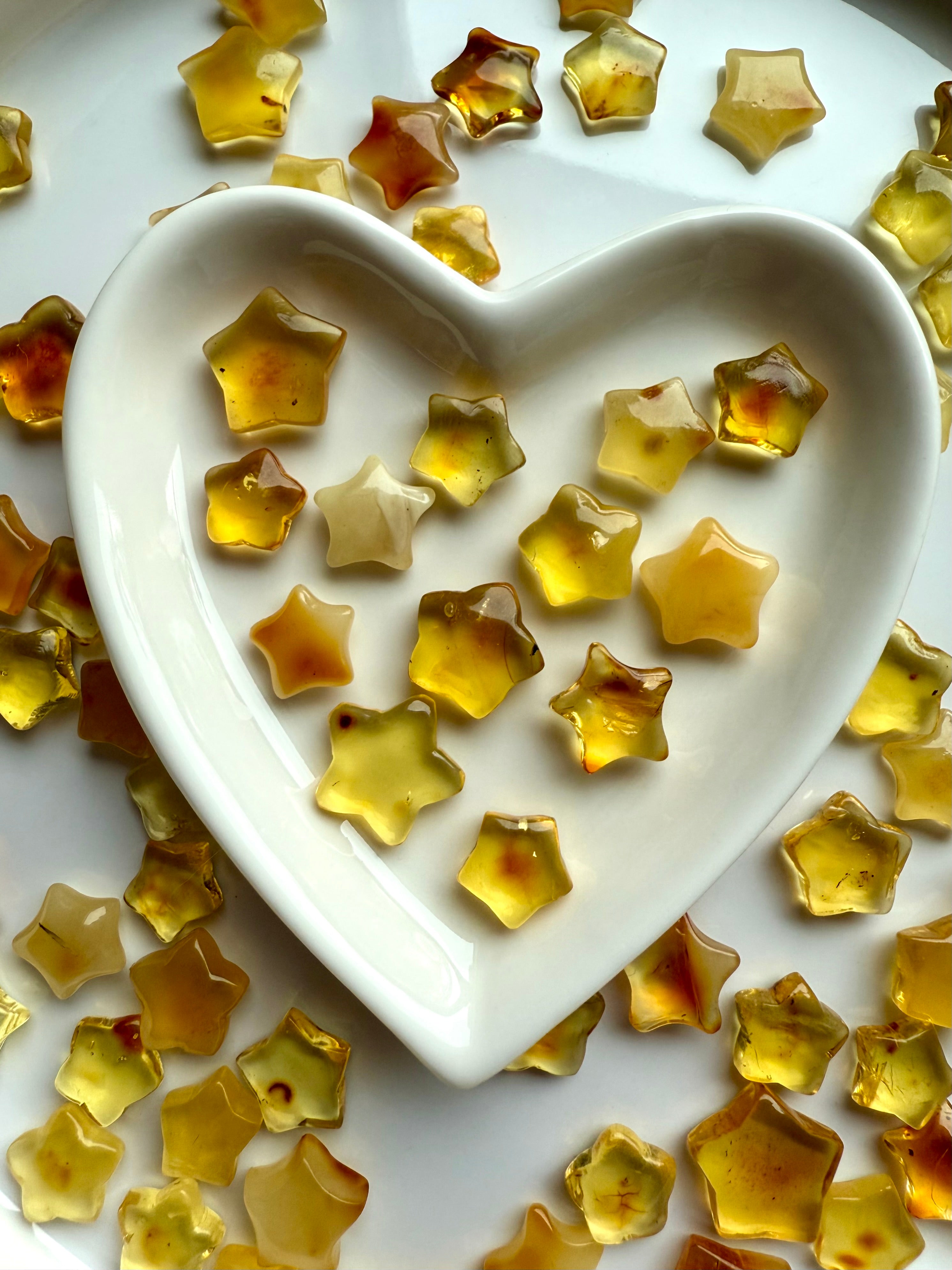 Golden Amber crystal star carvings in a white ceramic heart bowl with warm earthy hues – healing crystals for protection, vitality, and Solar Plexus chakra energy