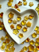 Golden Amber crystal star carvings in a white ceramic heart bowl with warm earthy hues – healing crystals for protection, vitality, and Solar Plexus chakra energy