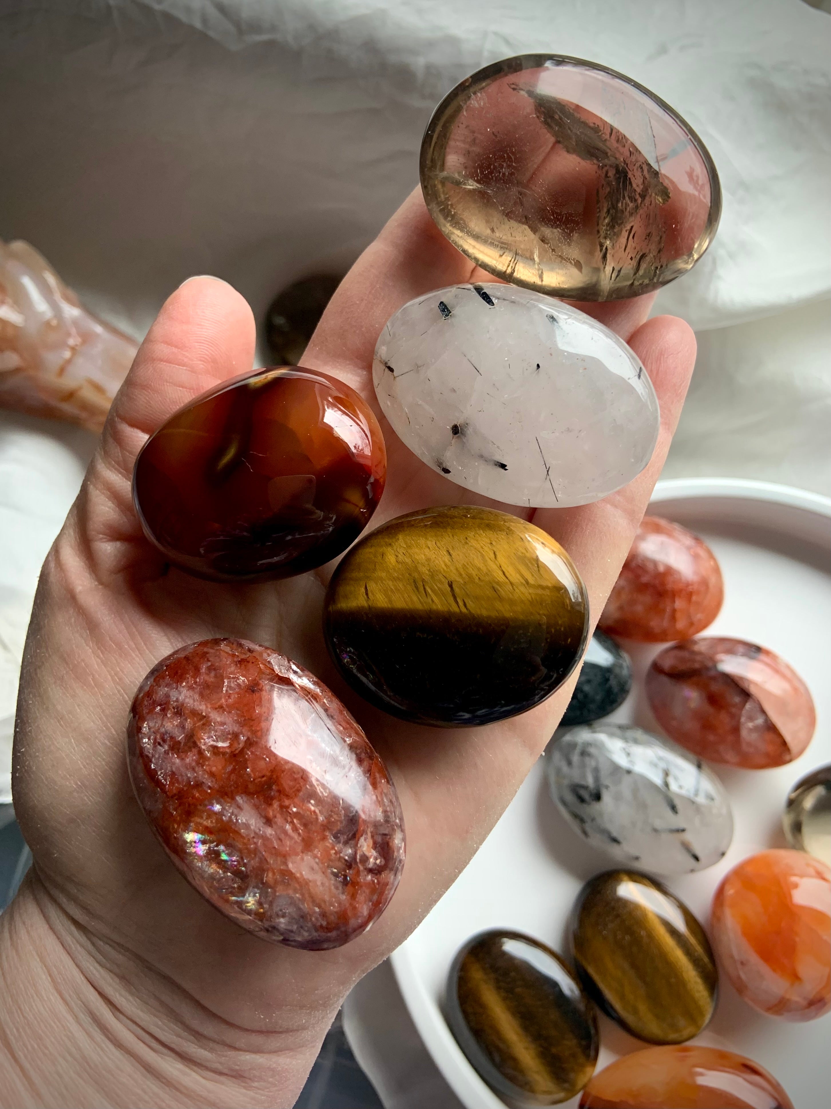 Chakra healing palm stones shown on hand with more stones in the background — polished crystals for grounding, motivation &amp; confidence.