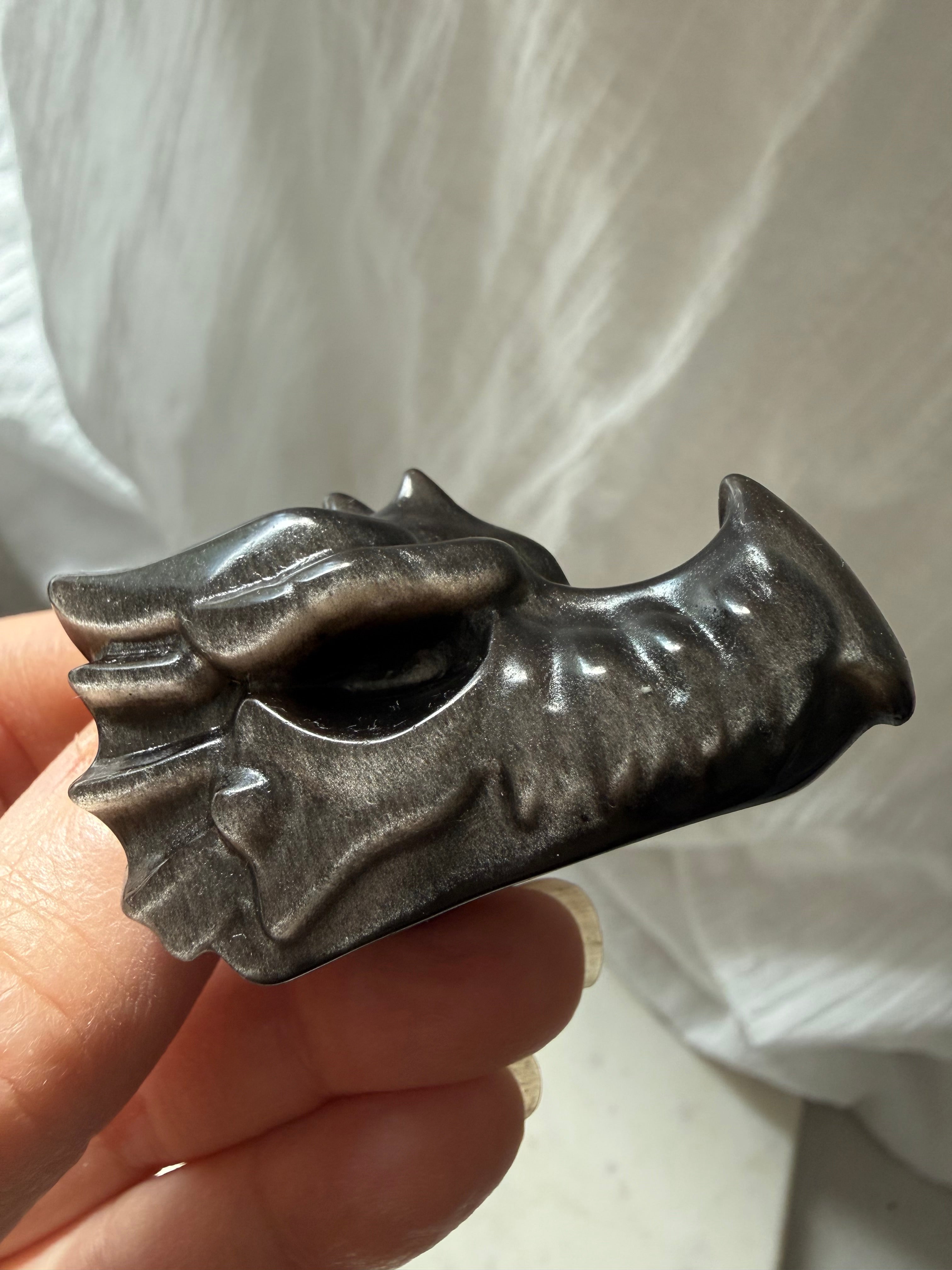 close-up of silver sheen obsidian dragon carving in hand highlighting polished surface and natural flash, stone for deep healing and protection