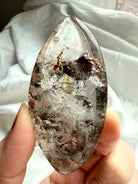 Garden Quartz marquise lens held in hand showing translucent crystal with scenic lodolite inclusions
