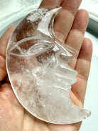 Clear Quartz Moon Face carving resting in hand, showcasing detailed carving on both sides and water-clear crystal clarity