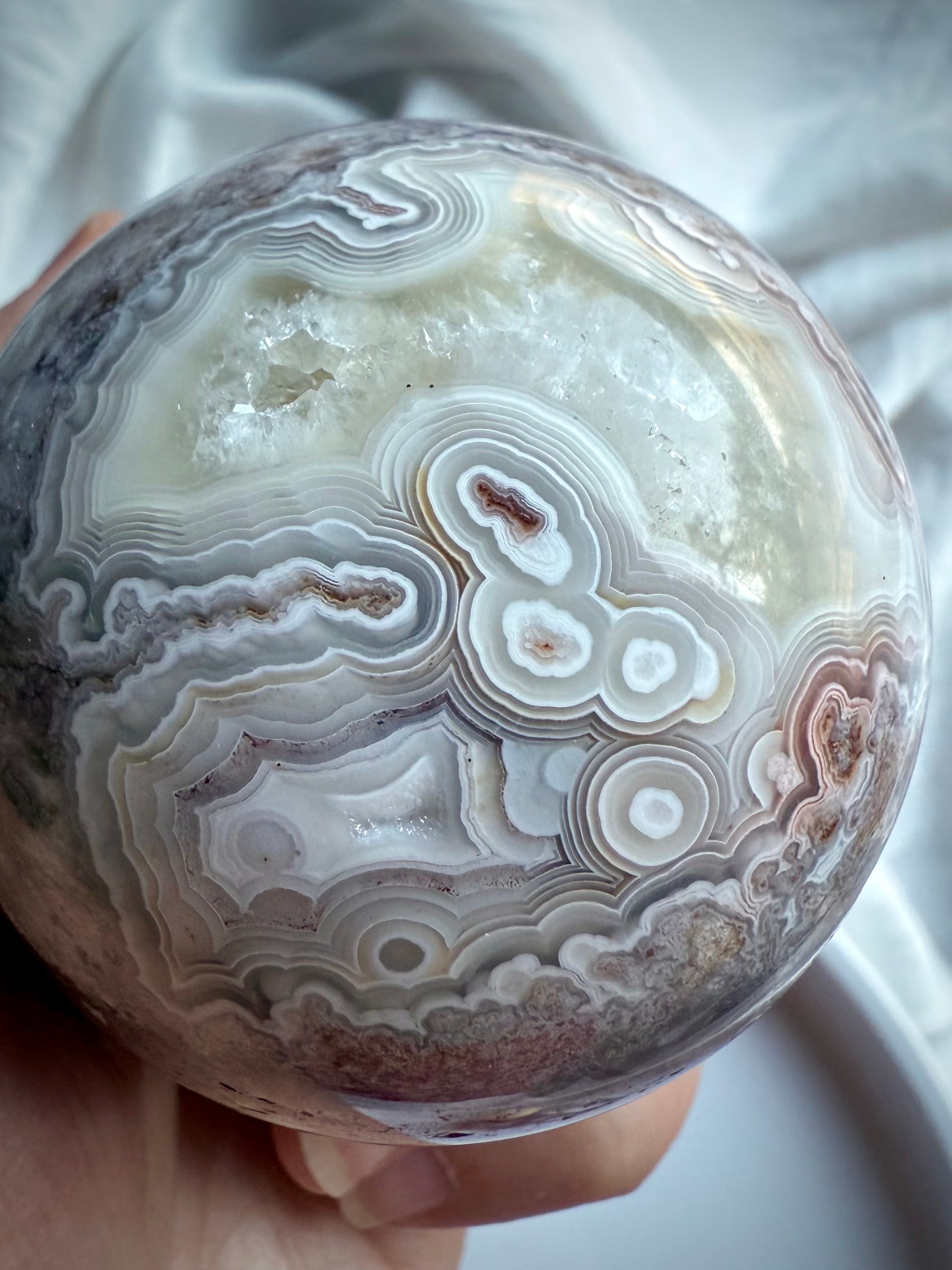 Close-up of Crazy Lace Agate sphere with creamy white banding, orbicular patterns, and exposed quartz window
