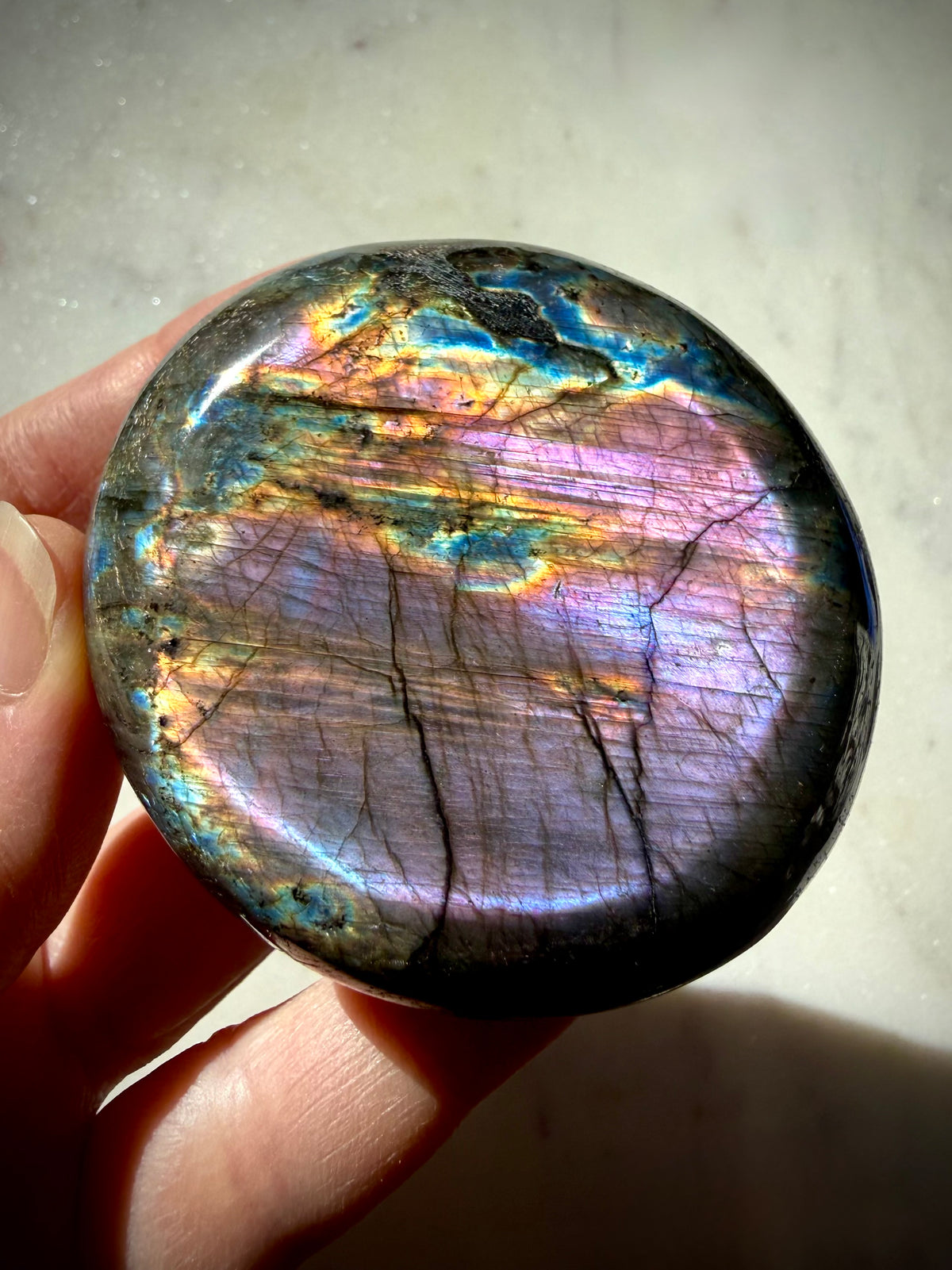 Violet Labradorite crystal held in hand with purple, blue and warm rainbow flash for intuition and Third Eye Chakra energy