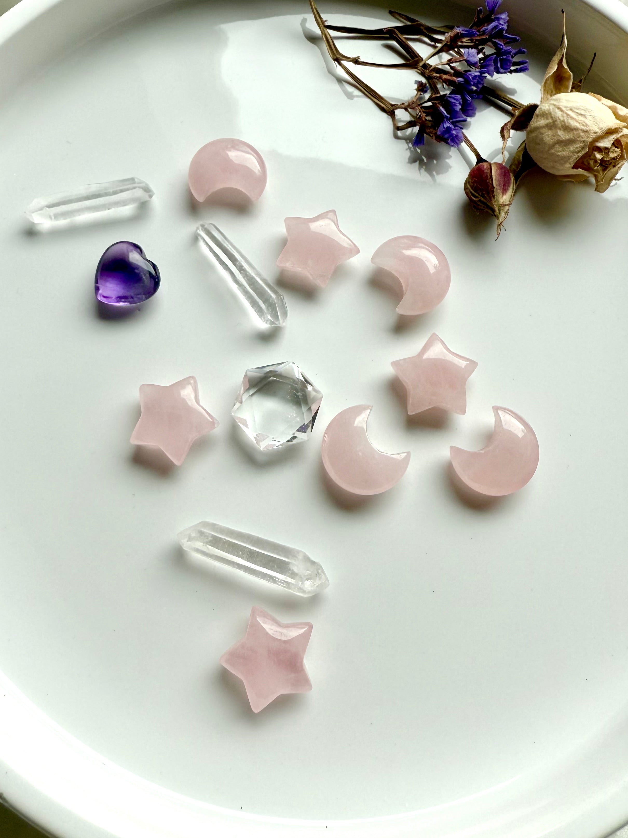 Array of mini Rose Quartz moons and stars with other crystals on a white plate. Soft pink carvings for Heart Chakra love, calm & emotional healing.