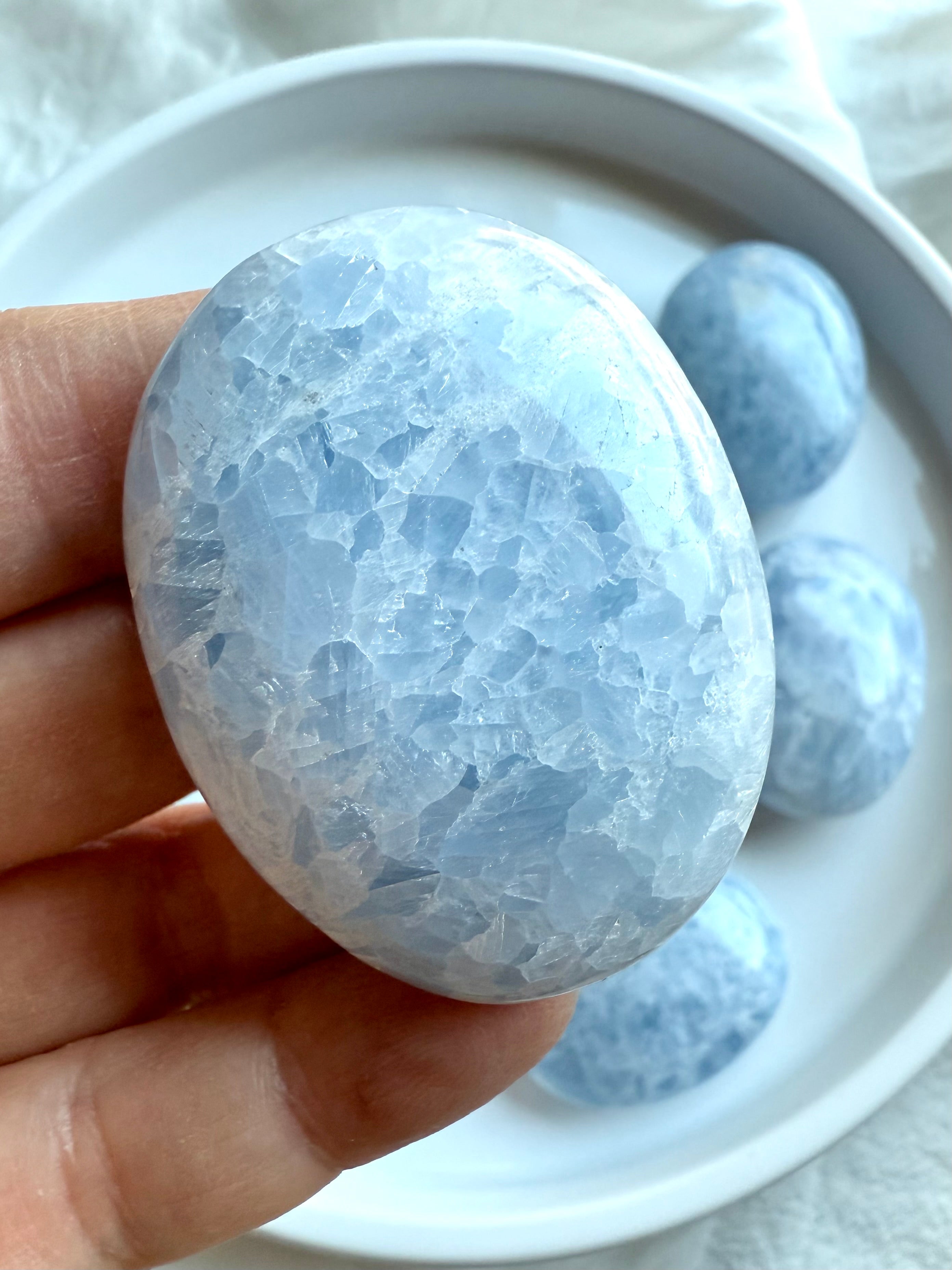 Macro shot of Blue Calcite palm stone — luminous surface with cloud-like inclusions and serene energy