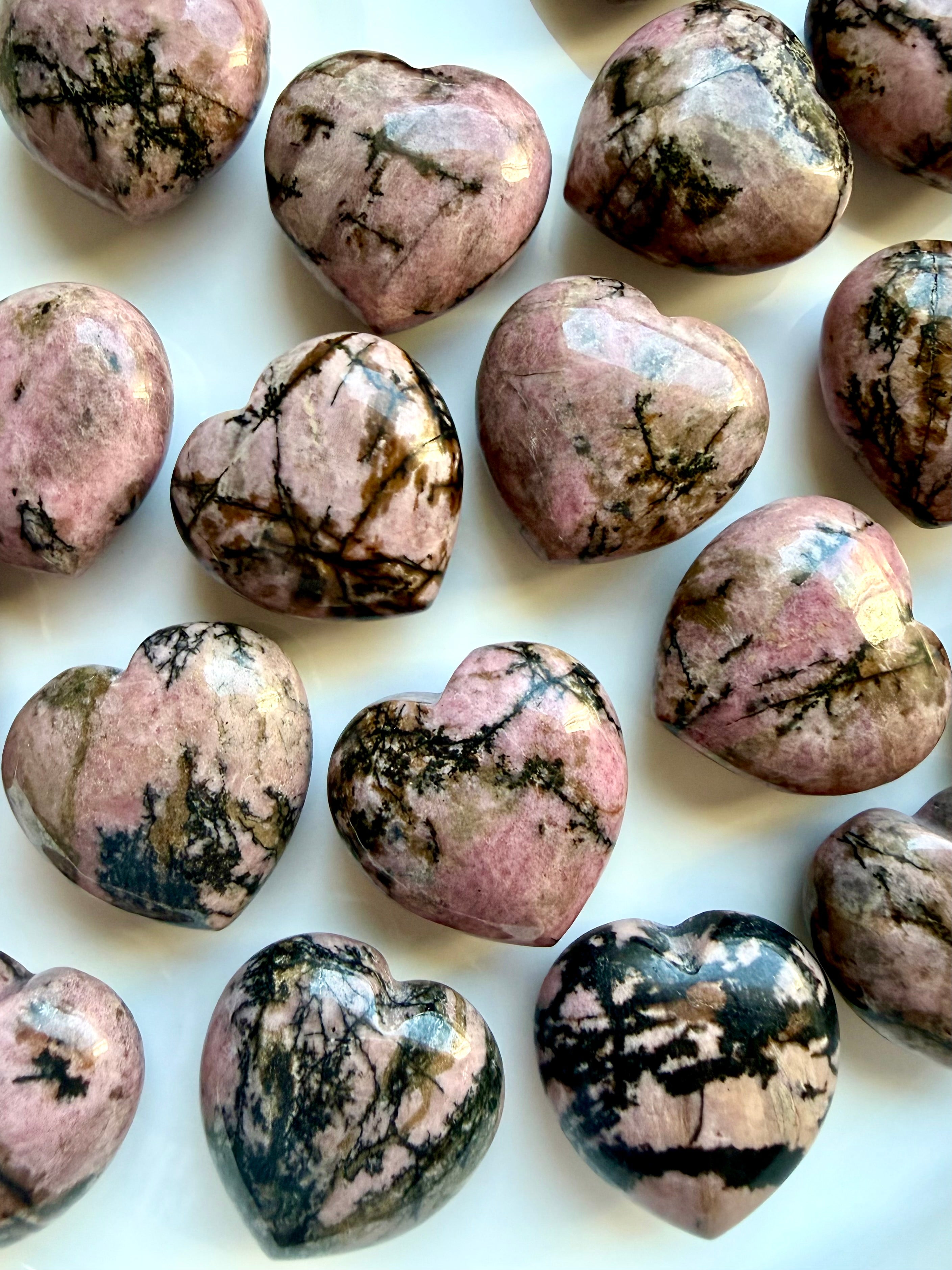 Assorted polished Rhodonite hearts displaying pink, black, cream and earthy mineral variations