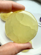 Lemon calcite disc held between fingers to show edge thickness and clarity