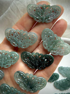 Blue Water Jade butterfly carvings in hand showing light, medium and dark jade color options