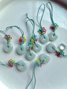 Group of natural jade donut charms with rainbow knot detail and green nylon cord shown on a white plate