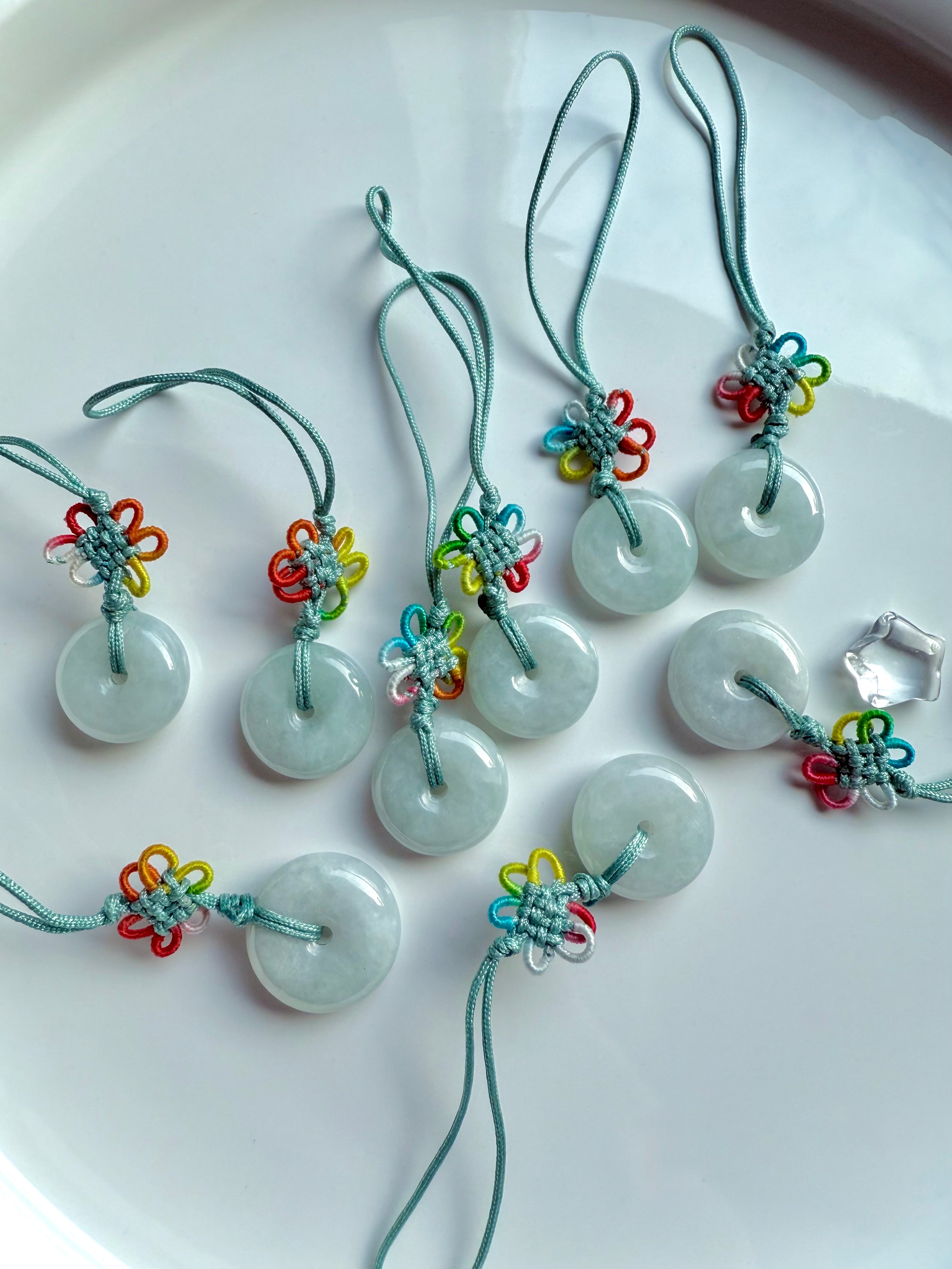 Group of natural jade donut charms with rainbow knot detail and green nylon cord shown on a white plate
