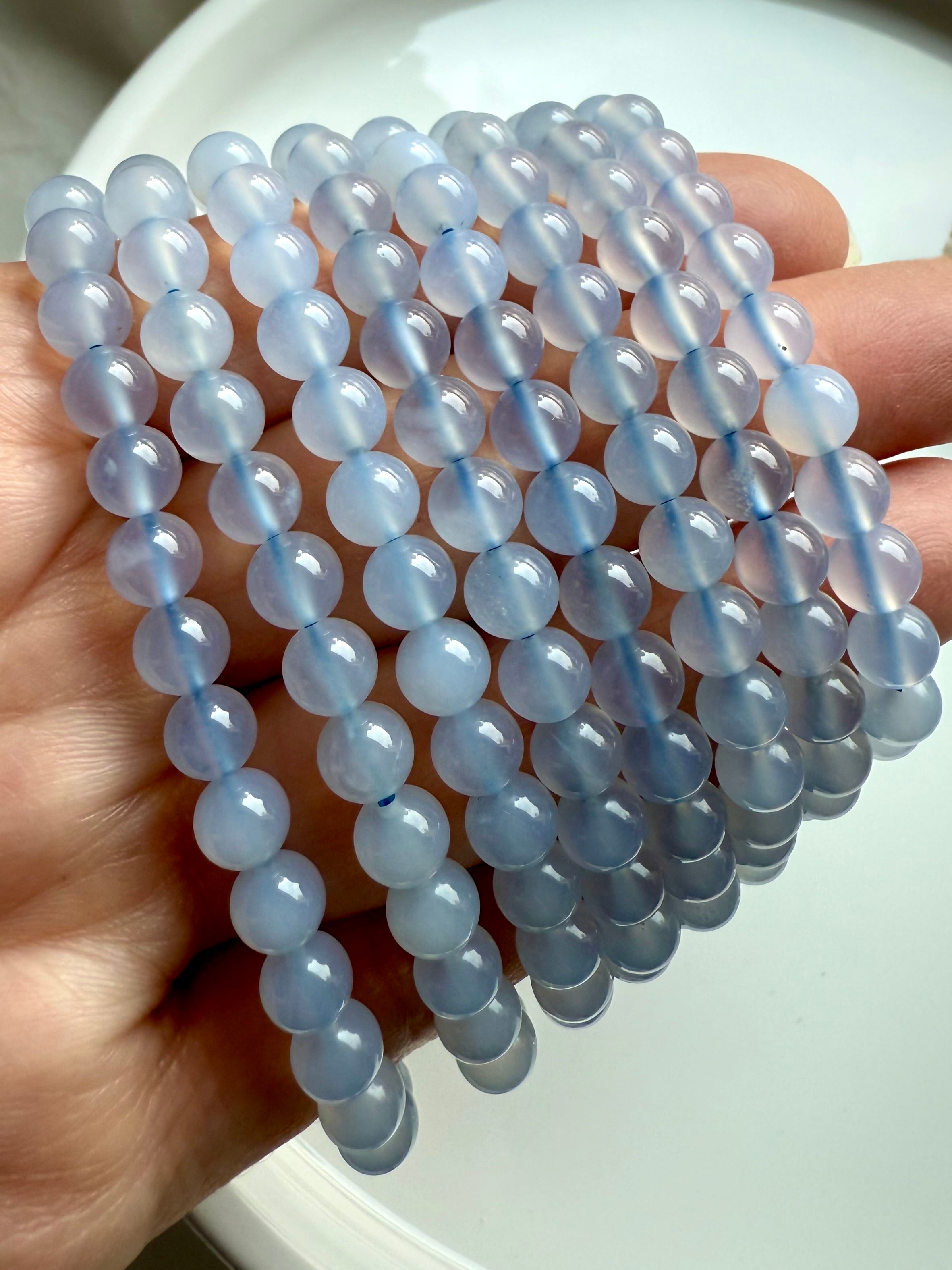 Layered Blue Chalcedony stretch bracelets fanned out in hand, showing polished round beads and dreamy blue tones