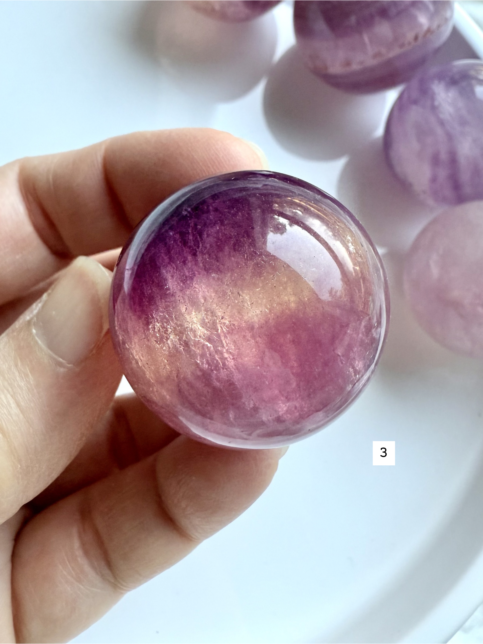 polished Candy Fluorite sphere with vibrant magenta and purple layers held in hand for intuitive energy
