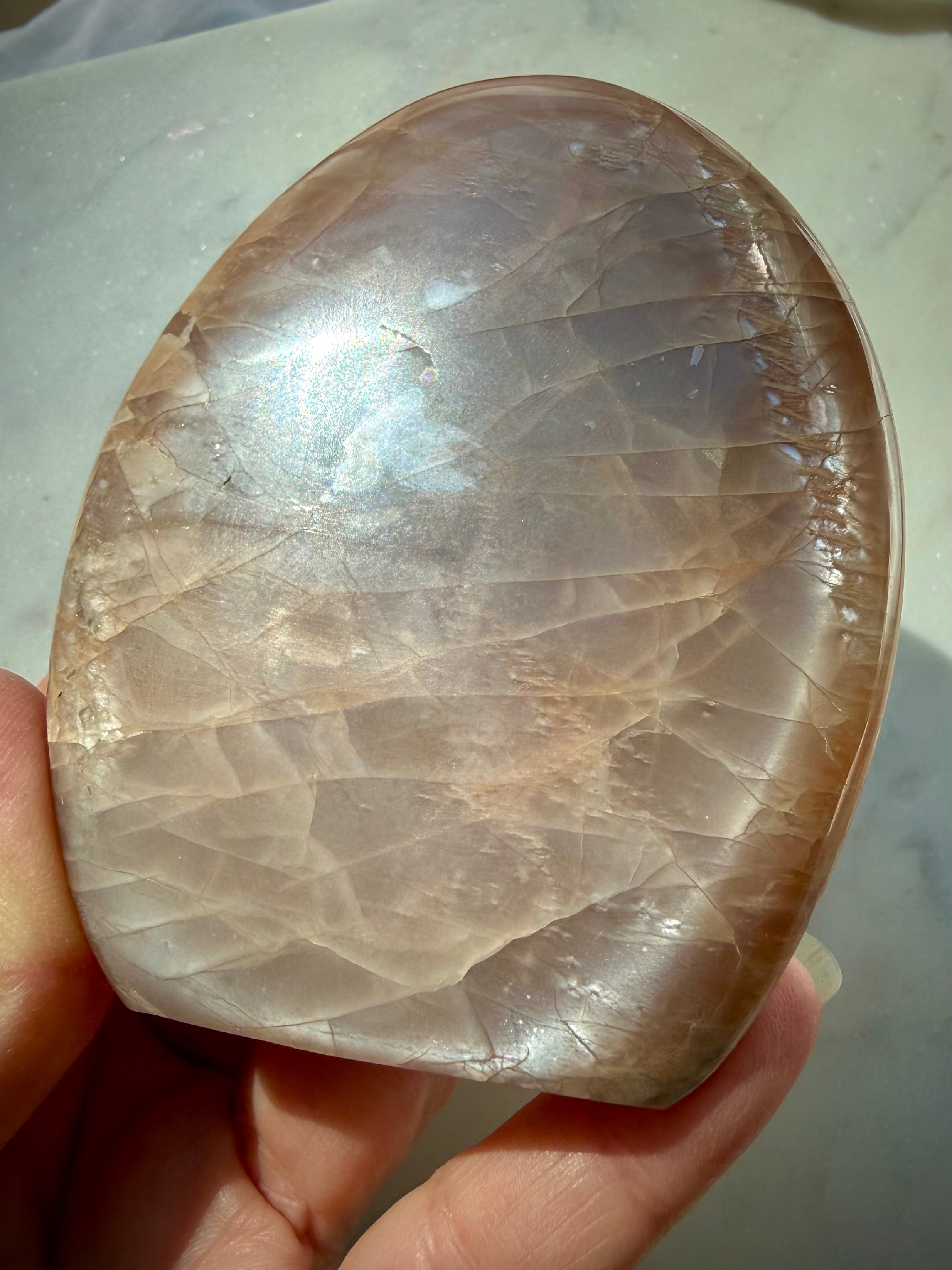 Peach Moonstone freeform held in hand with luminous silver flash, warm golden shimmer and natural rainbow iridescence