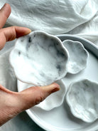 Close-up of hand holding a white marble daisy bowl showing natural gray and white stone patterning