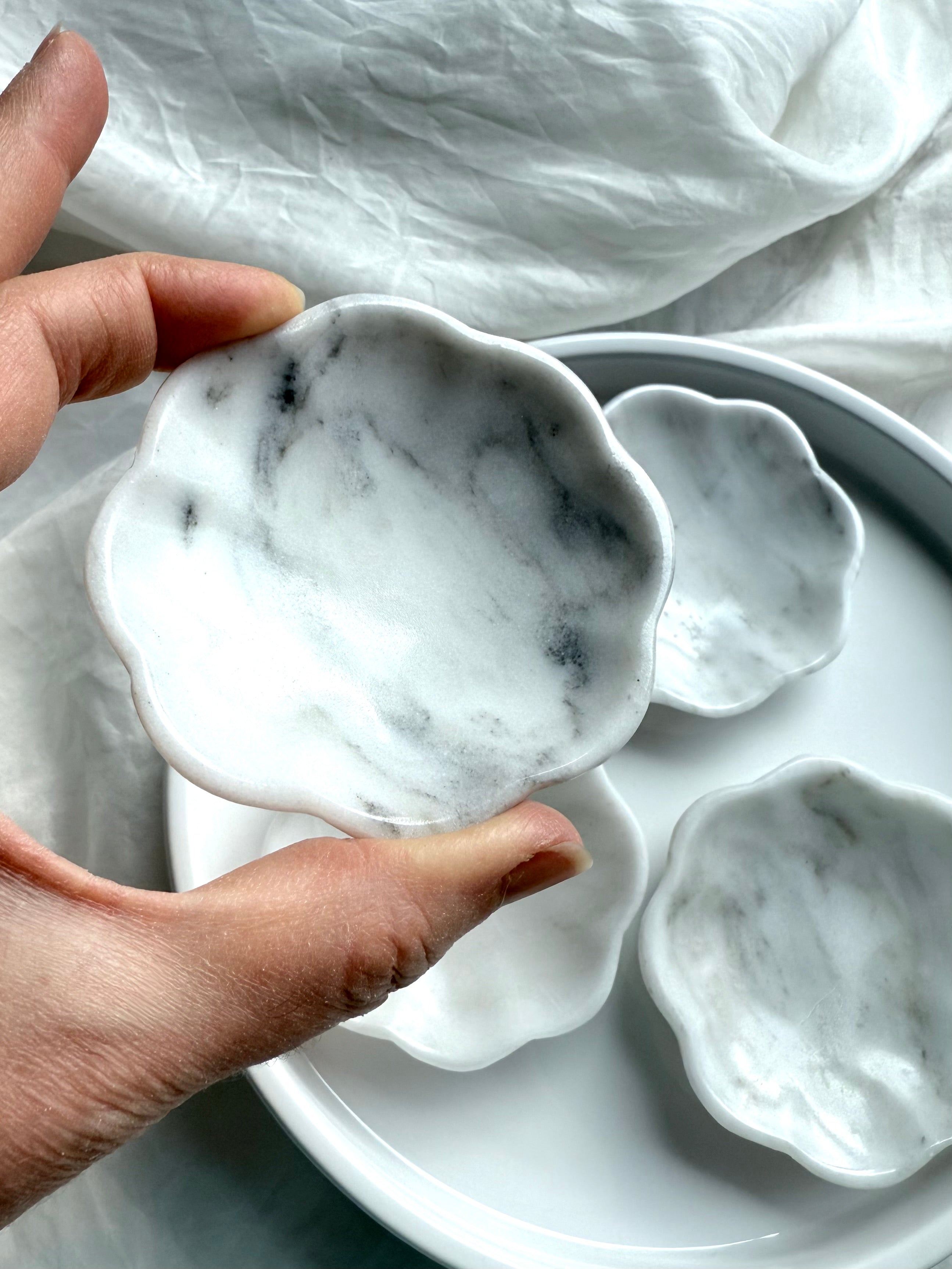 Close-up of hand holding a white marble daisy bowl showing natural gray and white stone patterning