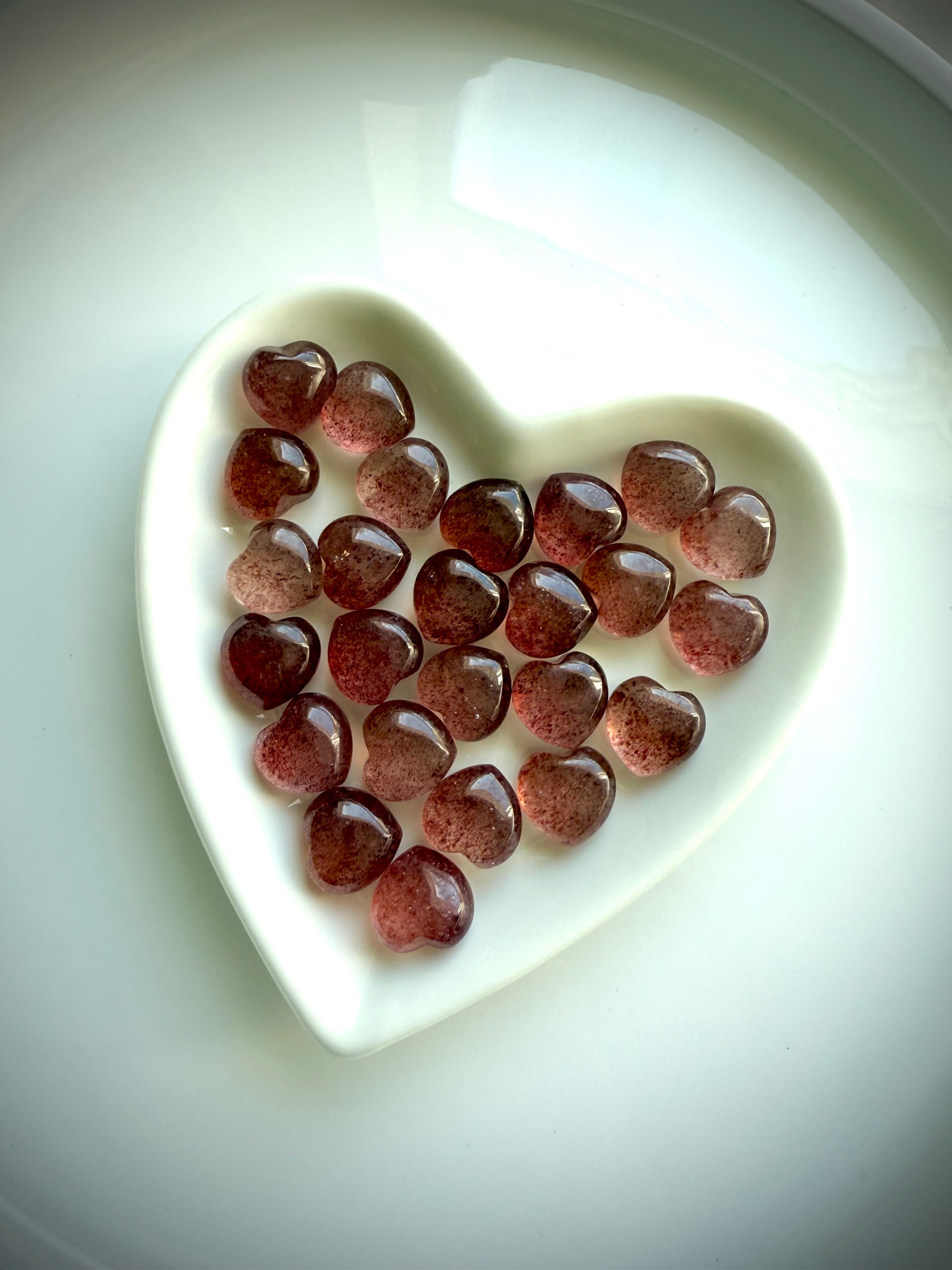 White ceramic heart-shaped bowl filled with Strawberry Quartz mini hearts — crystal gift idea for love, joy, and heart chakra support.
