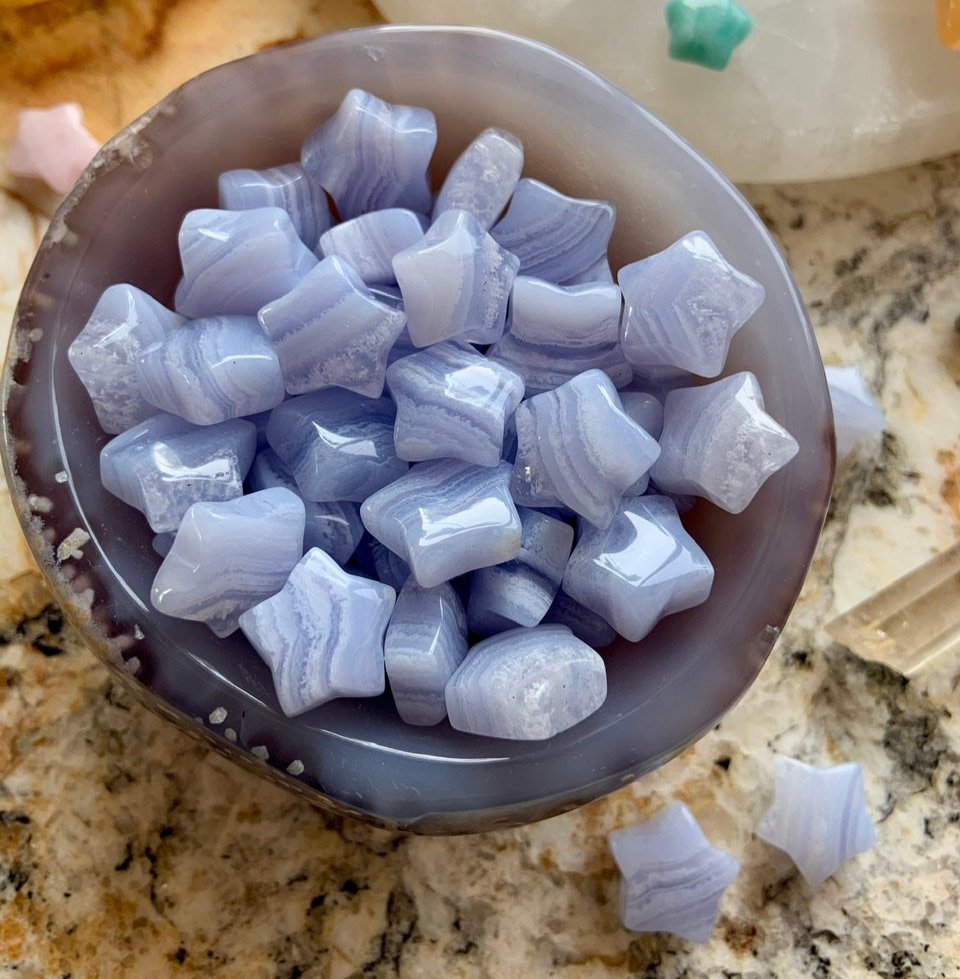 Close-up of blue/gray agate bowl filled with Mini Blue Lace Agate stars — soothing crystals for gentle communication & emotional peace.