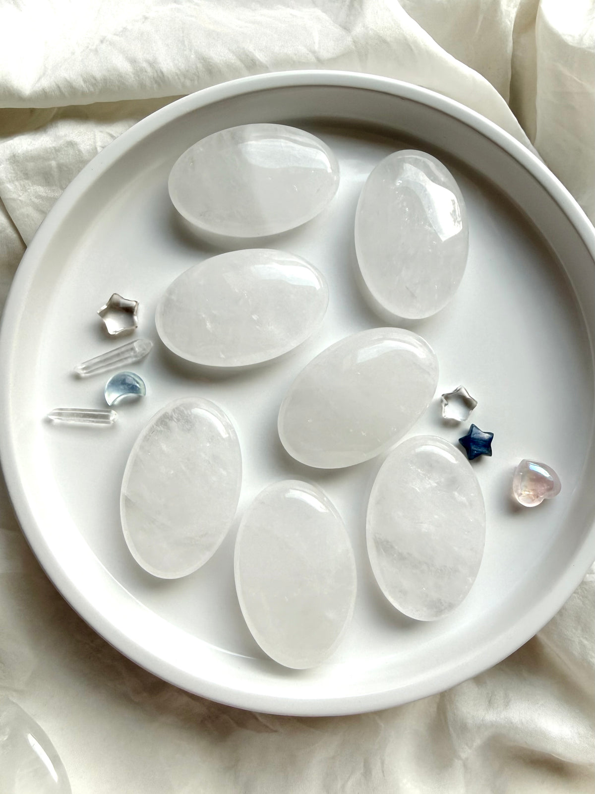 Clear Quartz palm stones arranged with tiny crystals showing smooth oval shapes, white veils and luminous polished surfaces