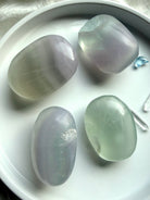 yttrium fluorite palm stones in soft pastel green and lavender tones on a white dish showing full assortment with natural banding and translucency