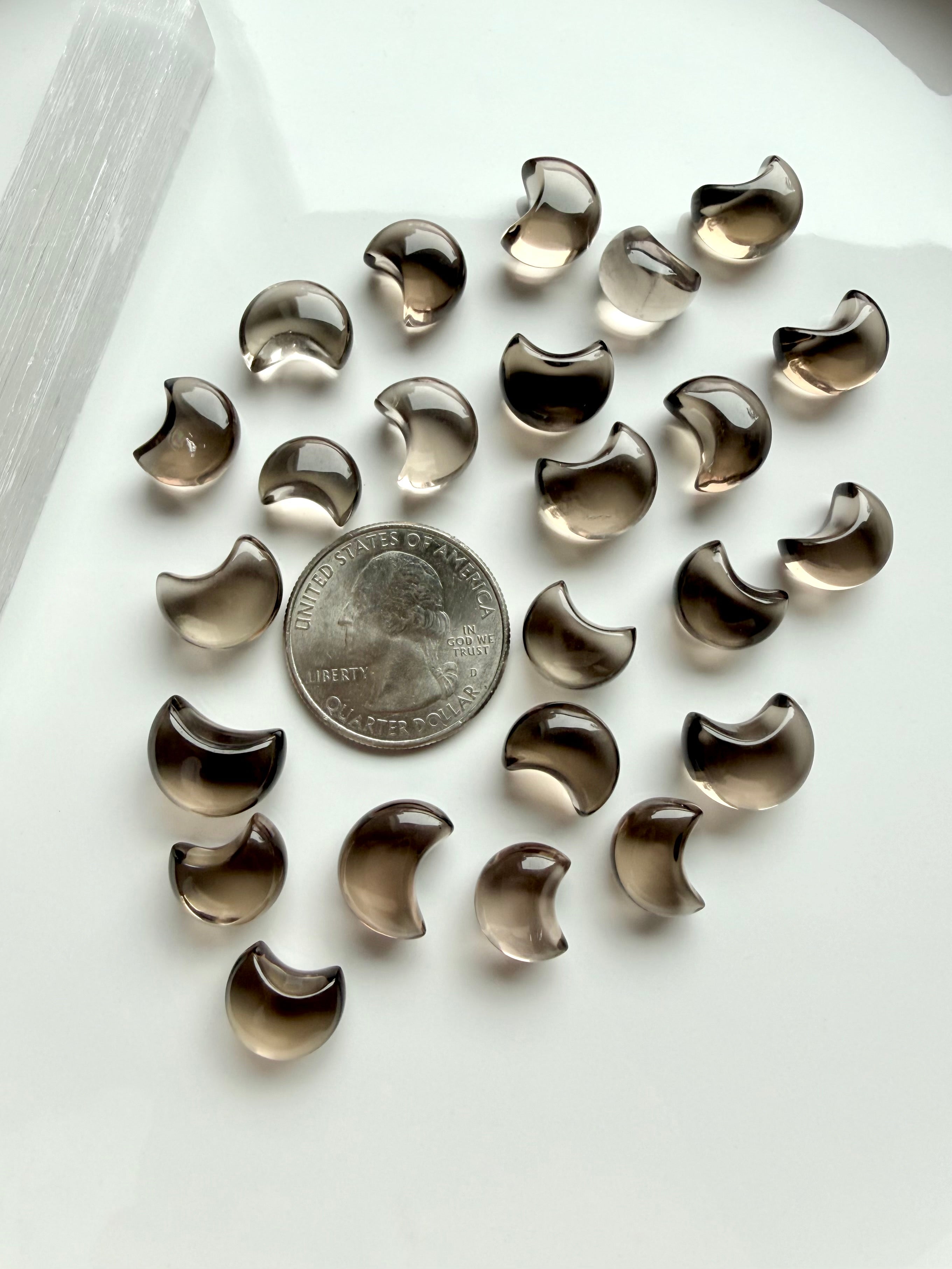 Smoky Quartz moon carvings next to a US quarter for scale, tiny crescent shapes with smoky brown tones and beautiful translucence