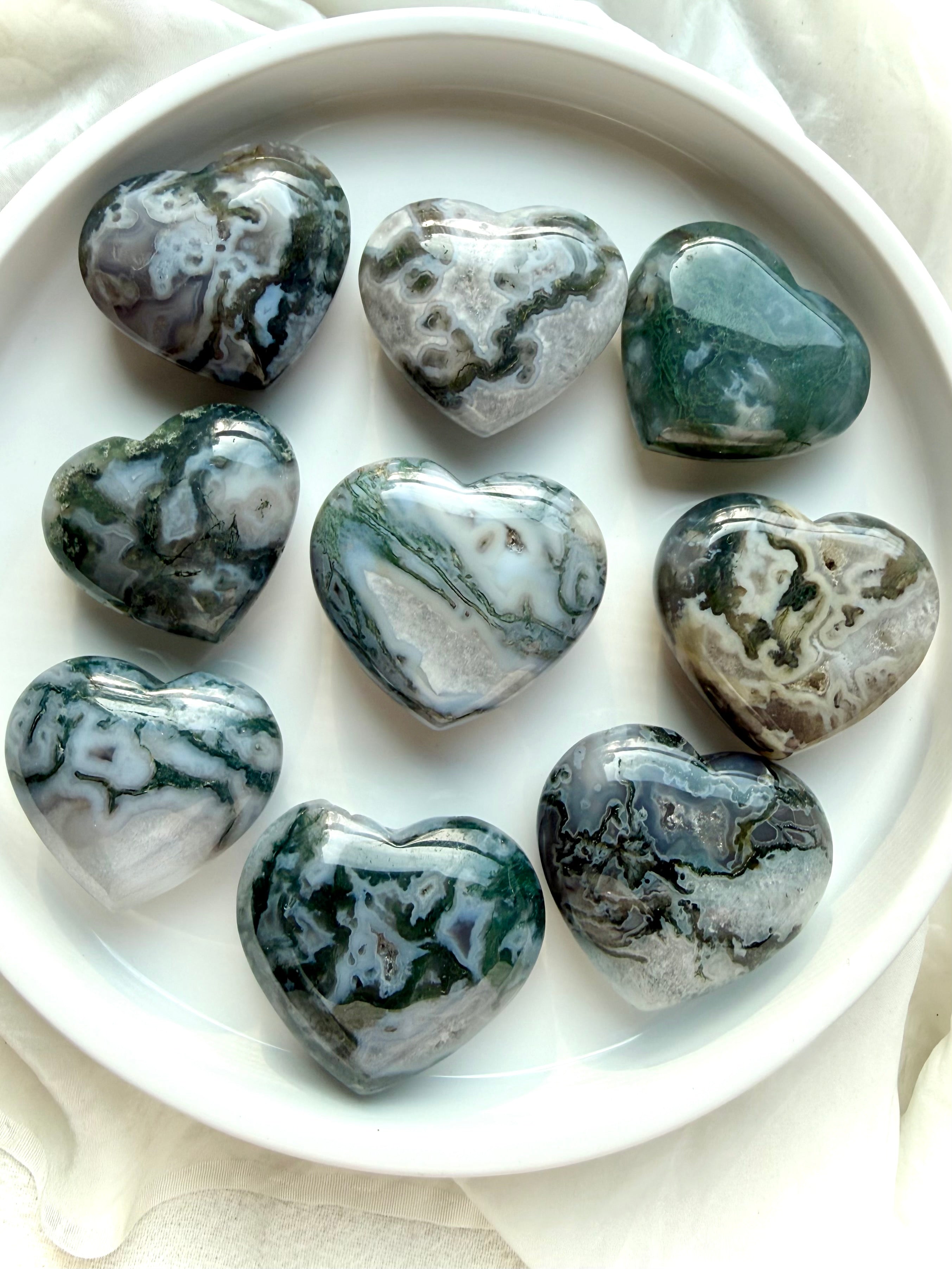 moss agate heart carvings on ceramic tray with natural green moss inclusions and polished crystal surfaces
