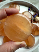 Polished honey calcite disc with golden translucence and subtle banding, held in natural light to highlight its radiant Solar Plexus energy.