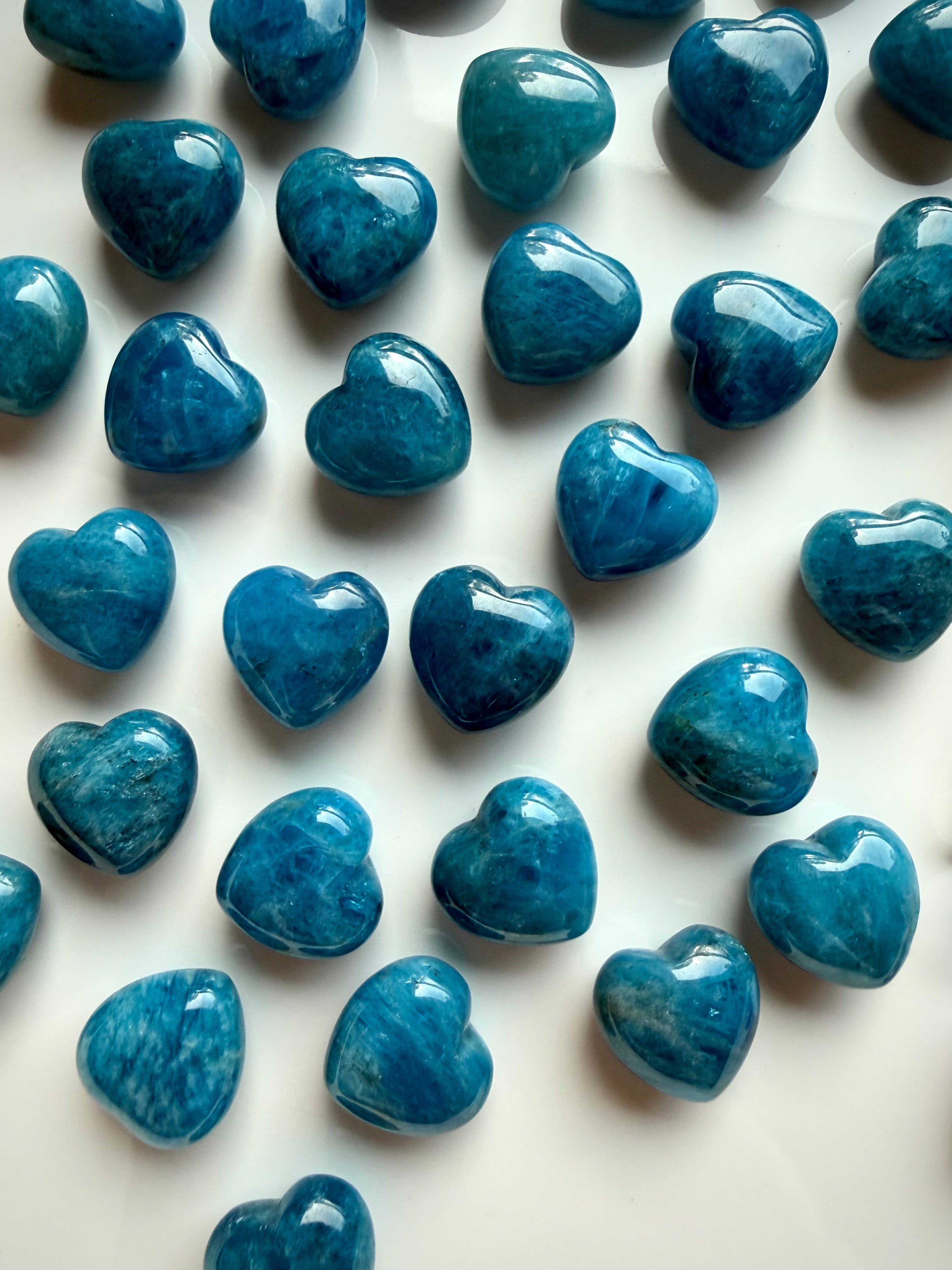 Mini Blue Apatite heart carvings arranged on white ceramic tray, polished blue crystal hearts for clarity, intuition and throat chakra healing 