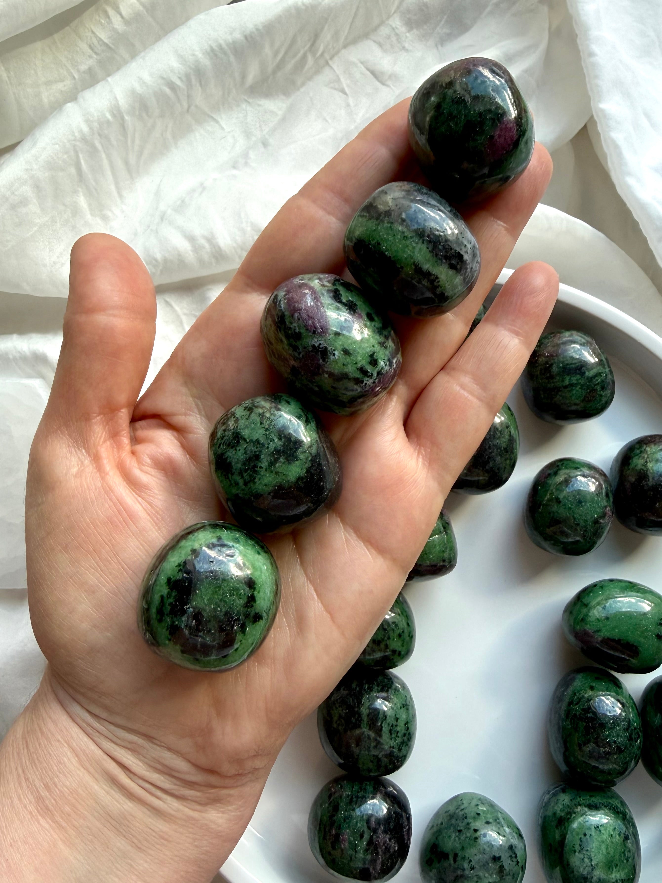 Ruby Zoisite healing crystals held in hand, polished green and ruby pink tumbled stones for passion, courage and emotional balance