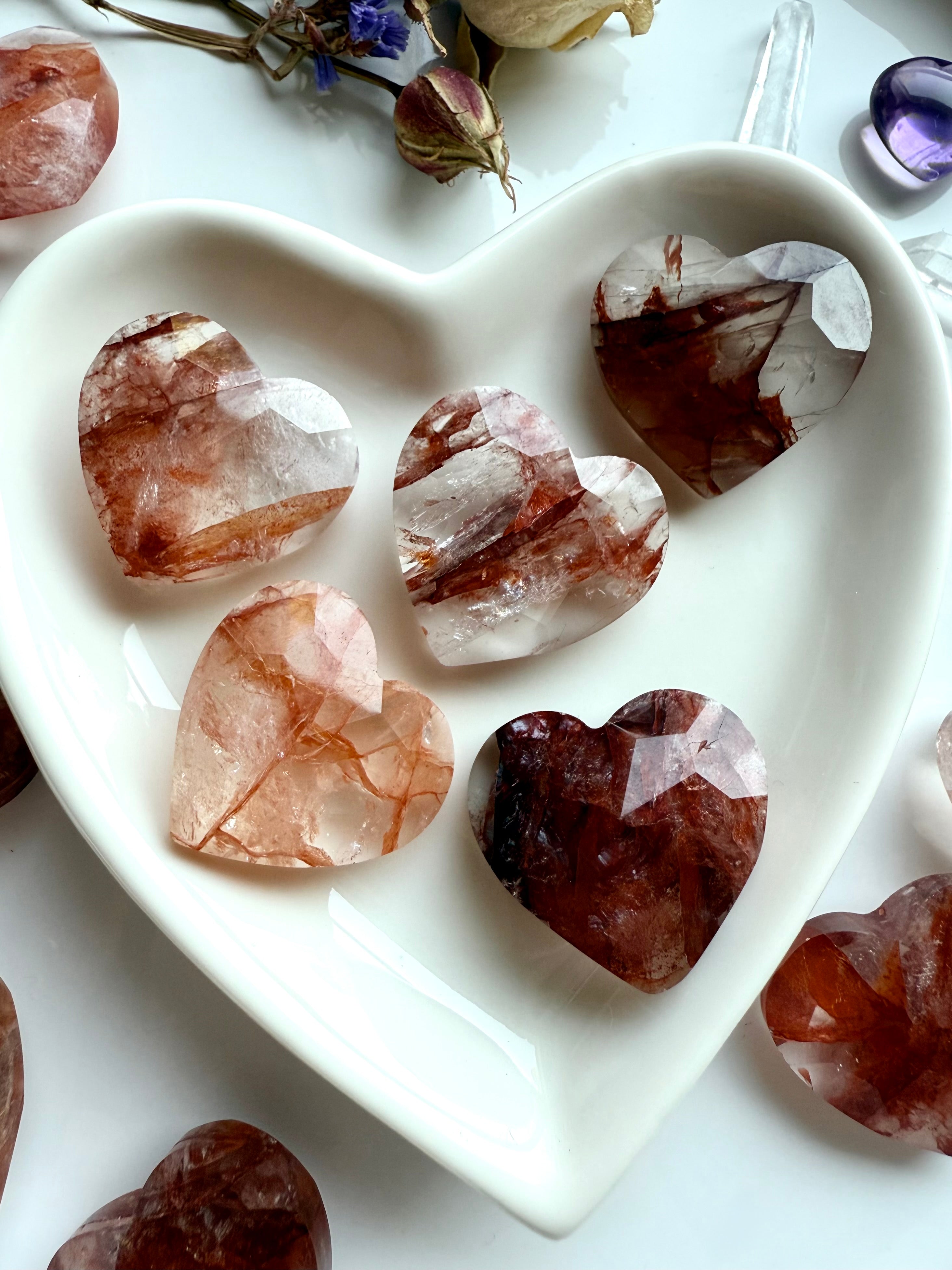 Close-up of faceted Fire Quartz hearts in a white heart bowl – polished hematoid quartz carvings for Root Chakra healing and energy clearing