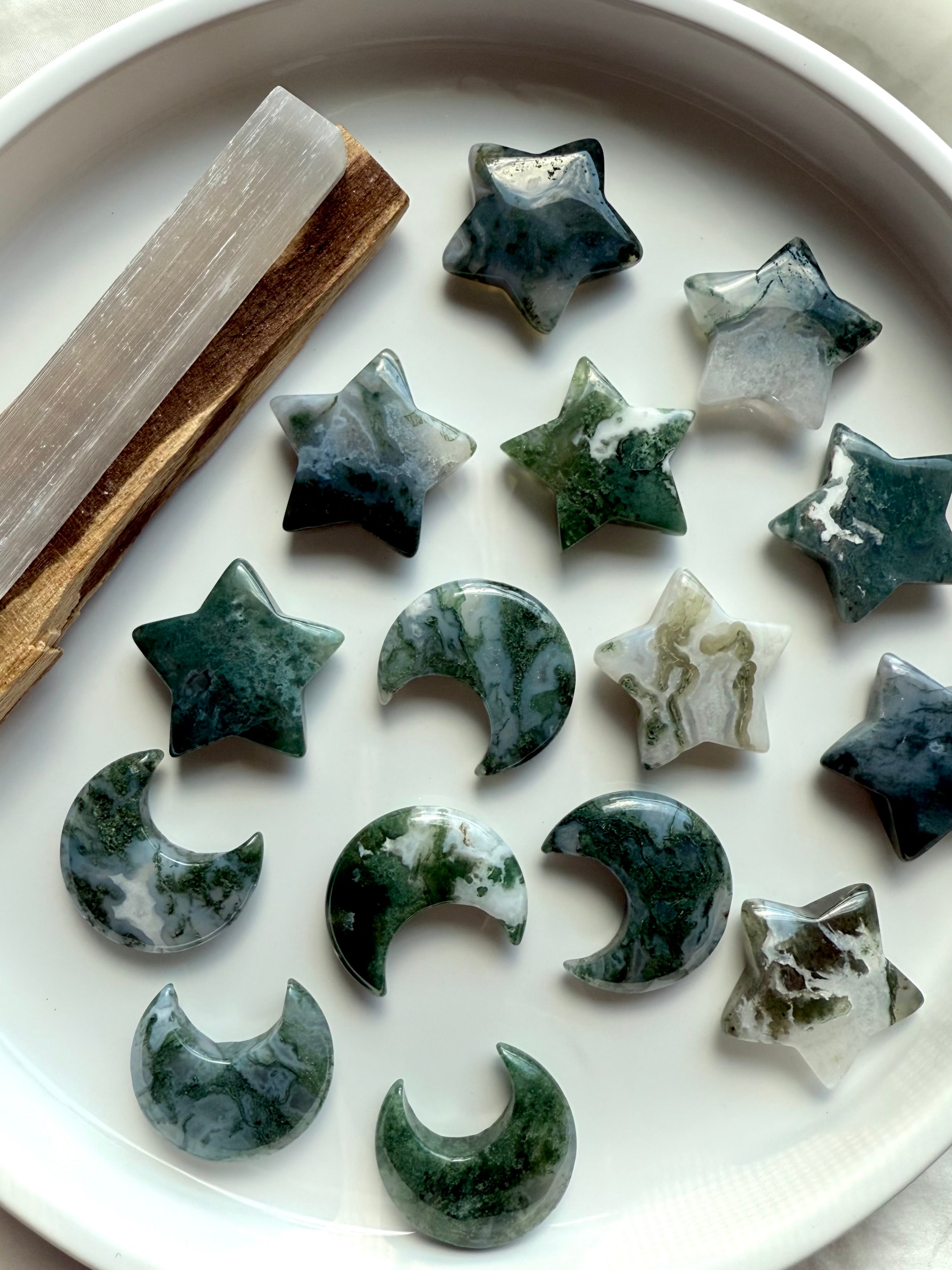Moss Agate stars and crescent moons displayed with selenite and palo santo — grounding crystal shapes for meditation, cleansing, and Earth connection rituals.