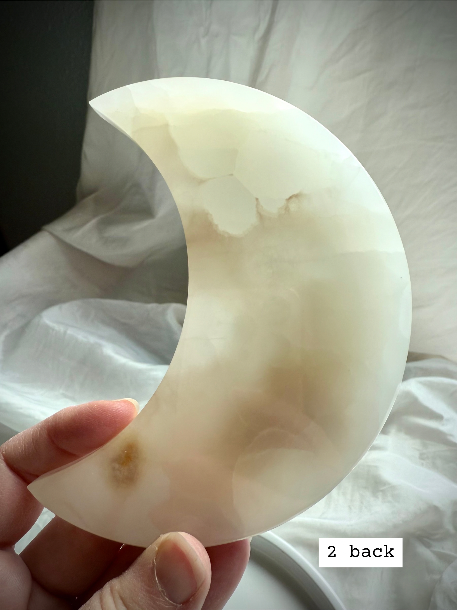 White Onyx Crescent Moon Plate held to the light showing pale creamy white and golden hues, back view.