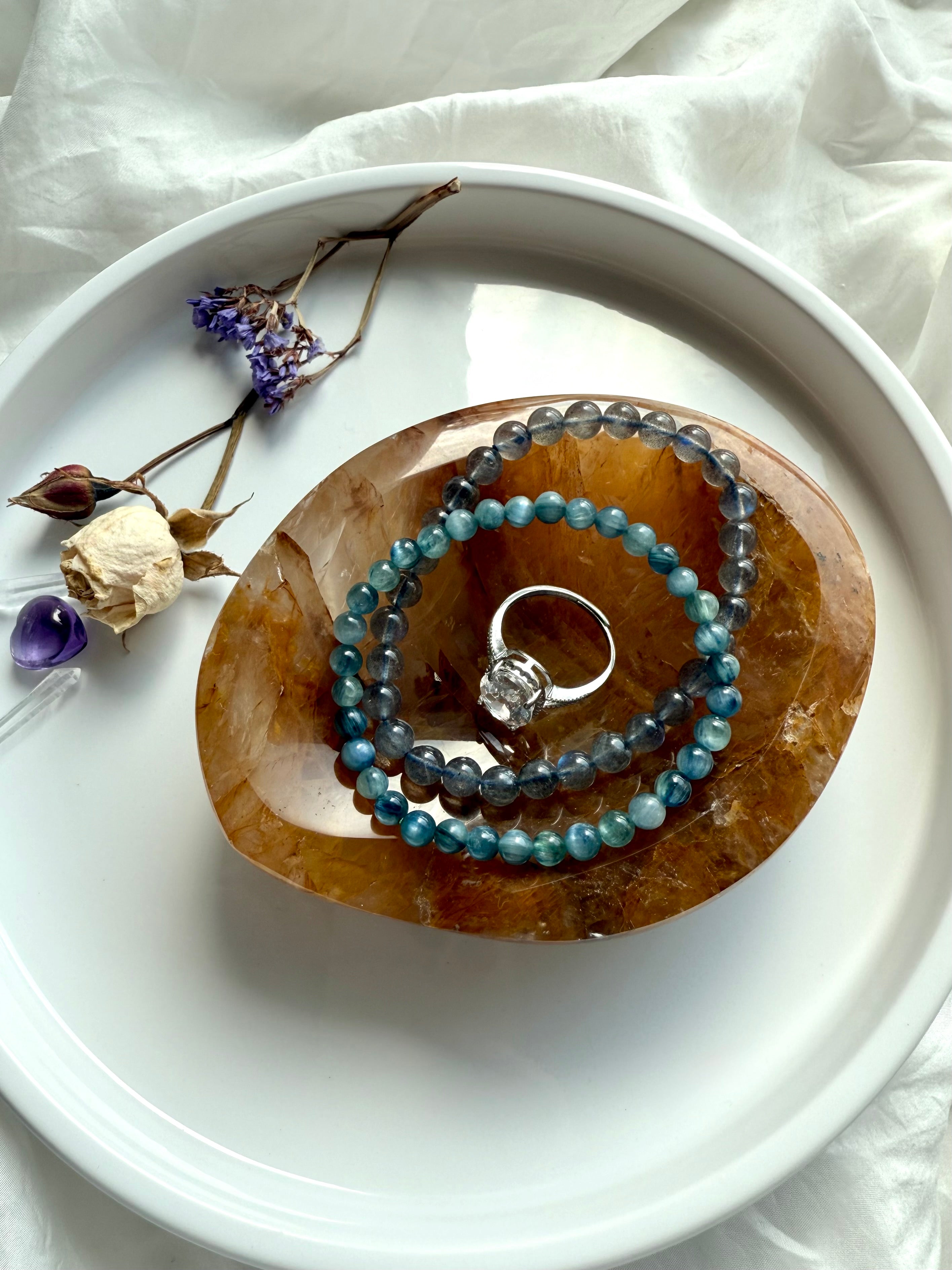 Golden Healer Quartz bowl as a crystal jewelry dish holding bracelets and a ring, styled with flowers and altar crystals on white plate