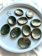 Pyrite worry stones arranged on a white dish with brilliant metallic luster and natural mineral variation