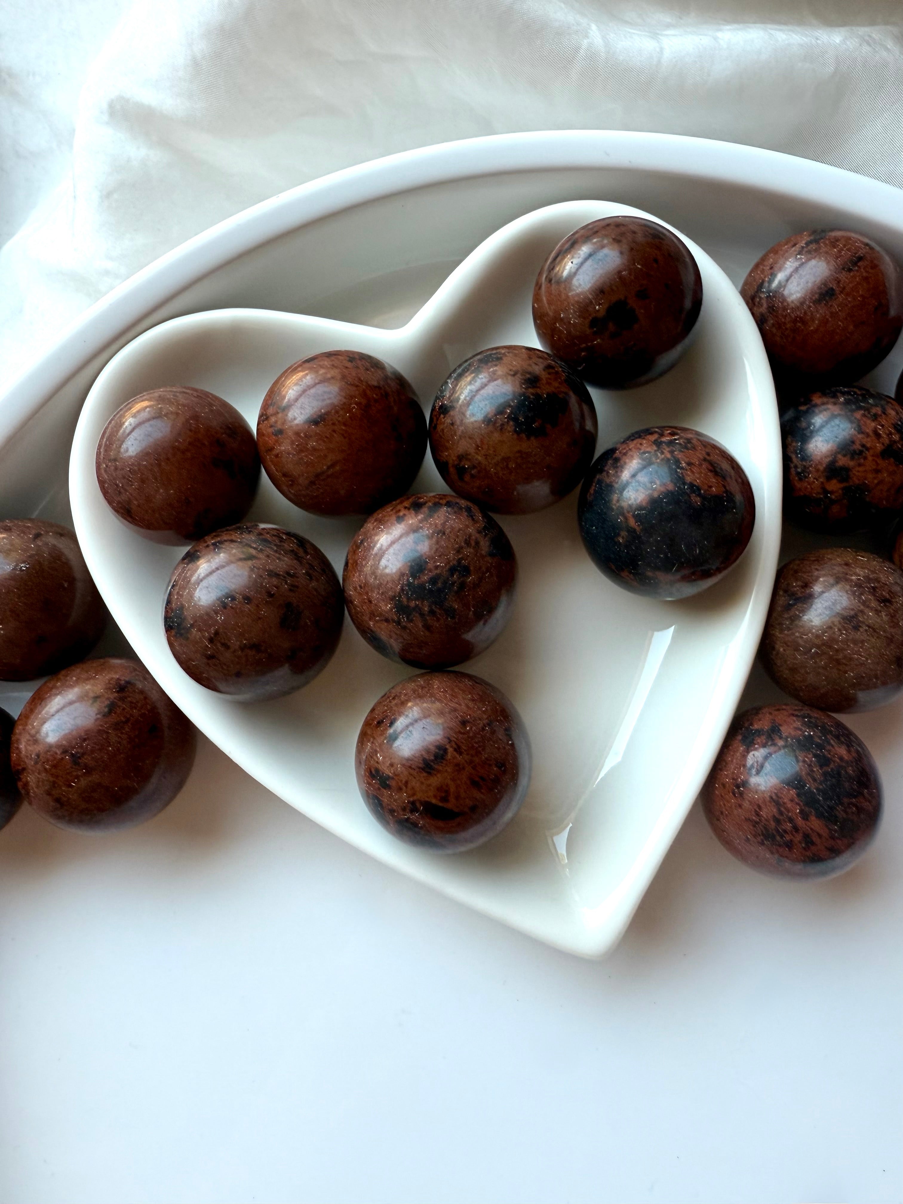 Polished Mahogany Obsidian crystal spheres displayed in white heart bowl – Root Chakra grounding stones