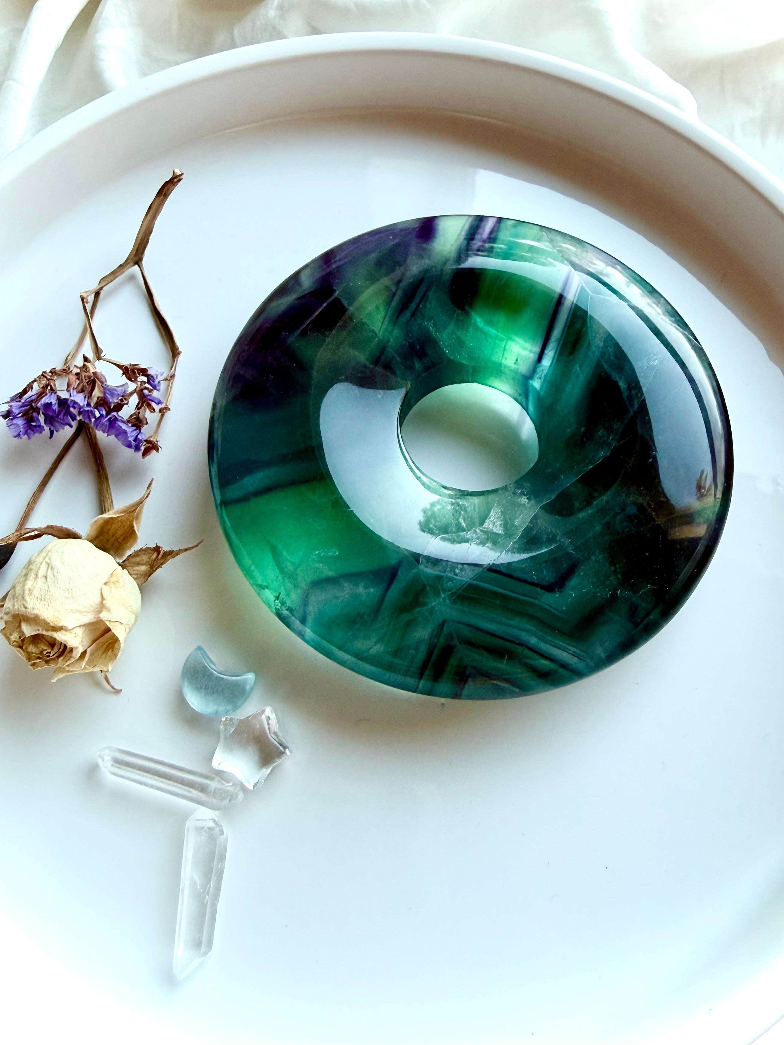 Angled view of a rainbow fluorite peace buckle donut on gold stand, highlighting translucent layers, crystal depth, and polished finish for altar or home decor