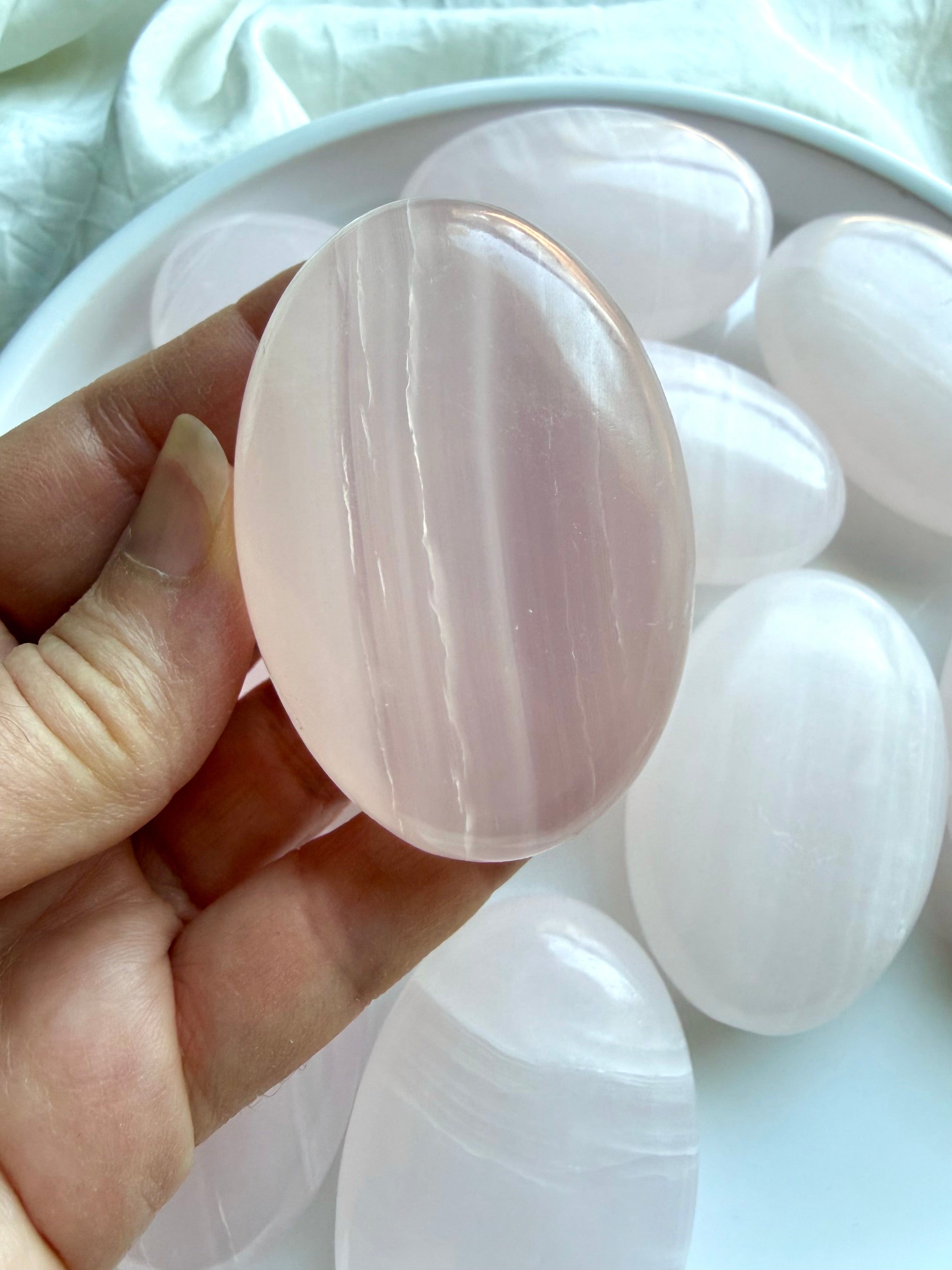 Mangano Calcite palm stone held in hand with creamy pink banding and polished natural finish