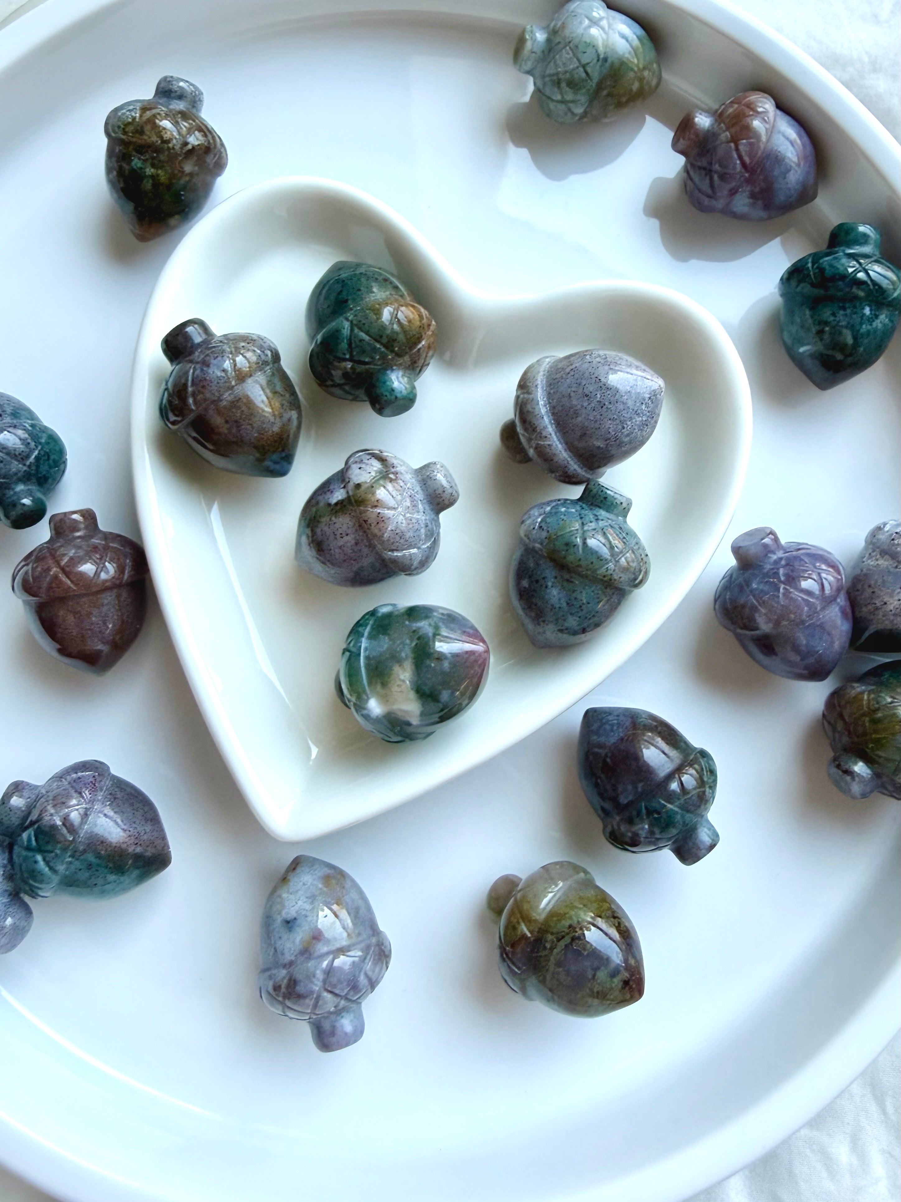 Mini Ocean Jasper acorns displayed in a white heart-shaped bowl showing varied teal, lavender, green and earthy natural patterns