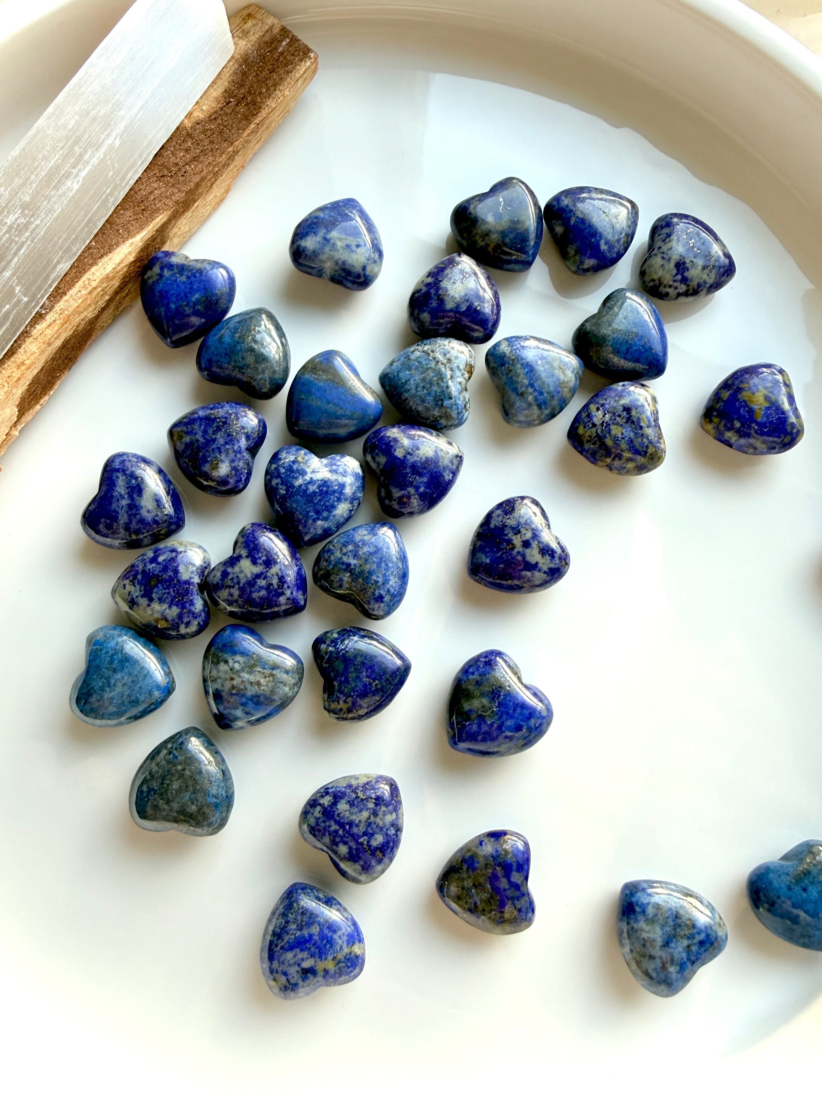 Mini Lapis Lazuli hearts arranged on a white tray, showcasing natural color variation and polished heart shapes, throat chakra healing crystals
