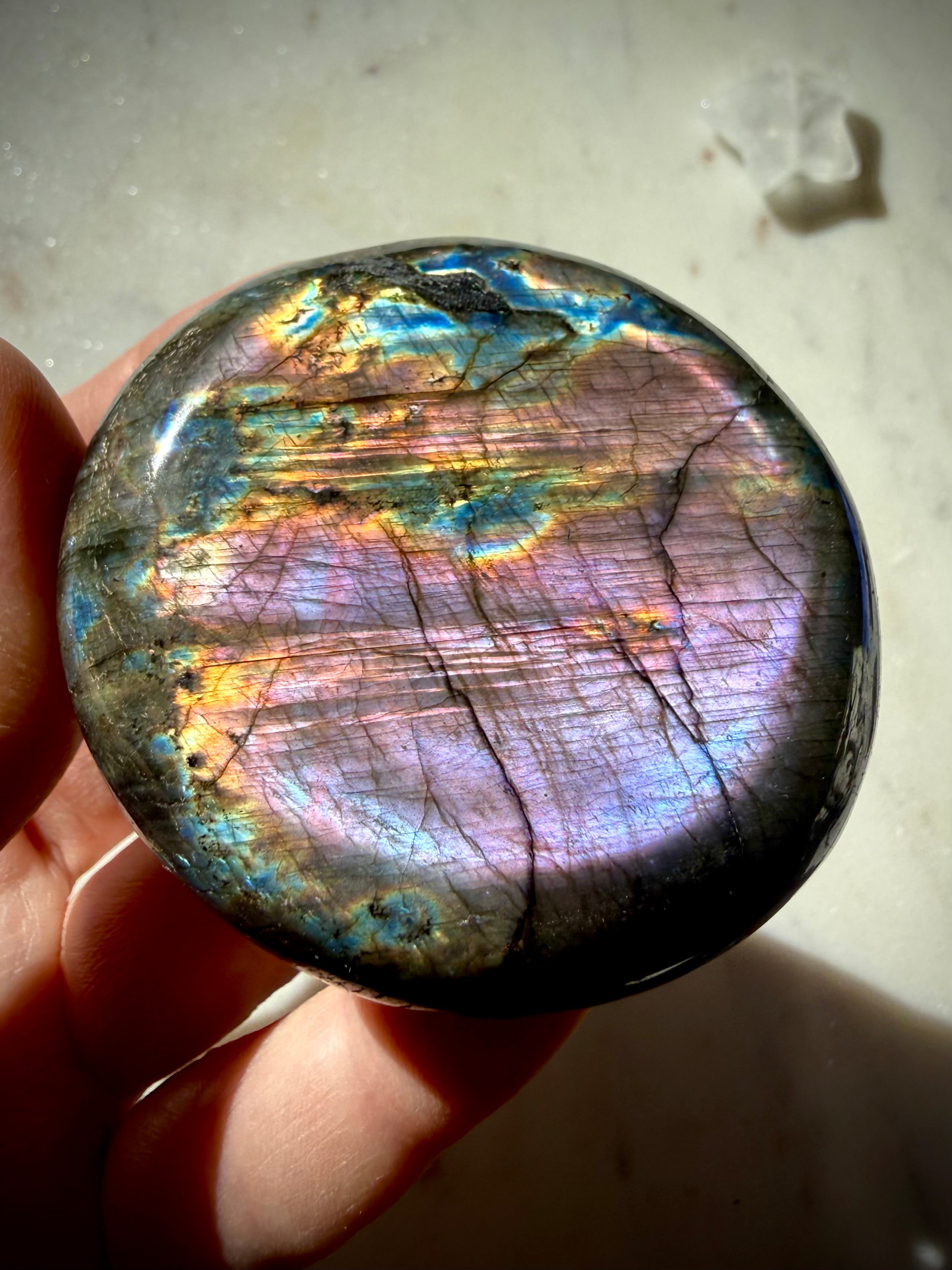 Purple Labradorite palm stone held in hand with luminous violet, pink, blue and gold rainbow labradorescence