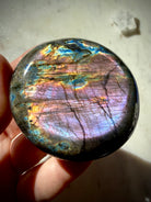 Purple Labradorite palm stone held in hand with luminous violet, pink, blue and gold rainbow labradorescence