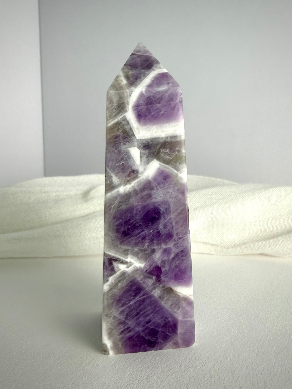 Chevron Amethyst tower standing upright, featuring rich violet crystal formations, white quartz bands and a polished pointed termination