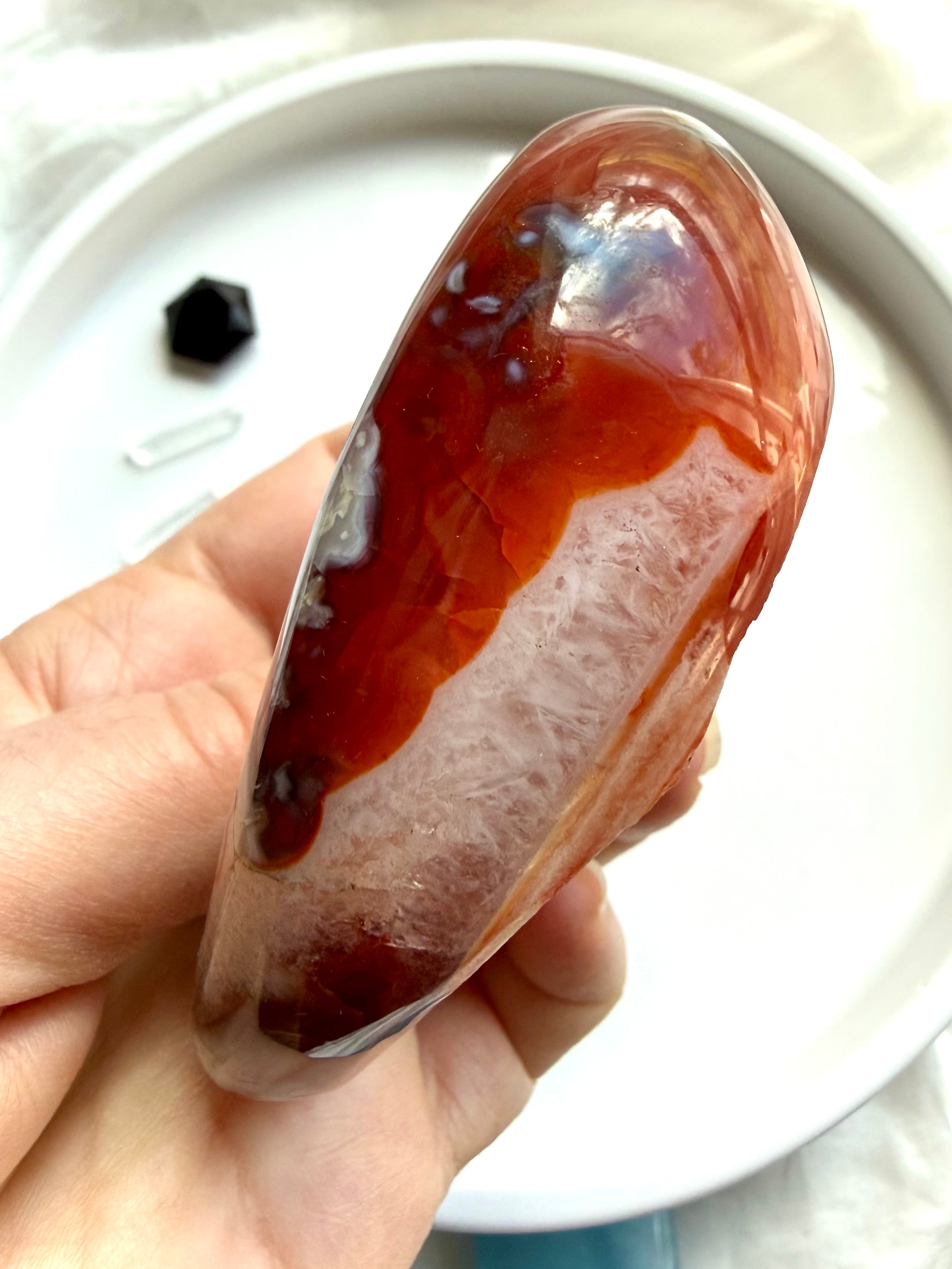 side view of polished carnelian stone bowl with quartz pattern and banded agate detail in hand