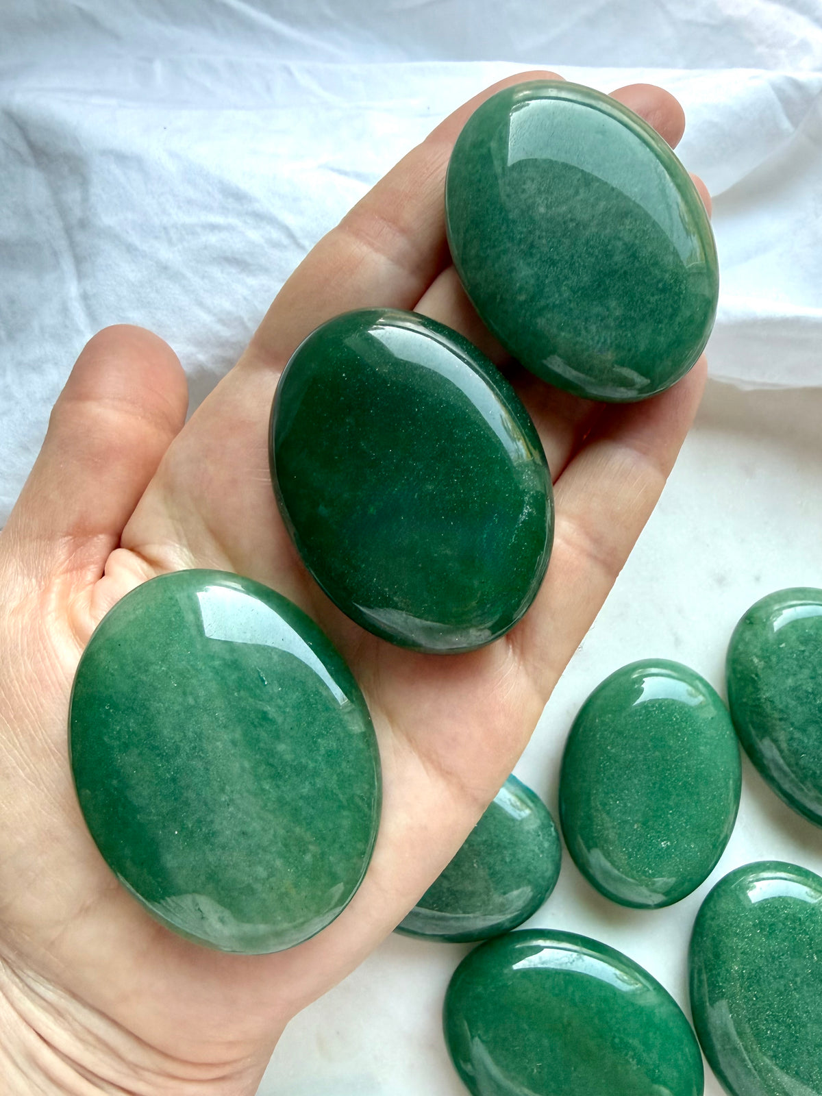 Green Aventurine palm stones held in hand showing polished oval shapes, size, and natural color variation