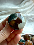 Mini Polychrome Jasper palm stone with earthy brown, cream, and forest green color zoning, held between fingers