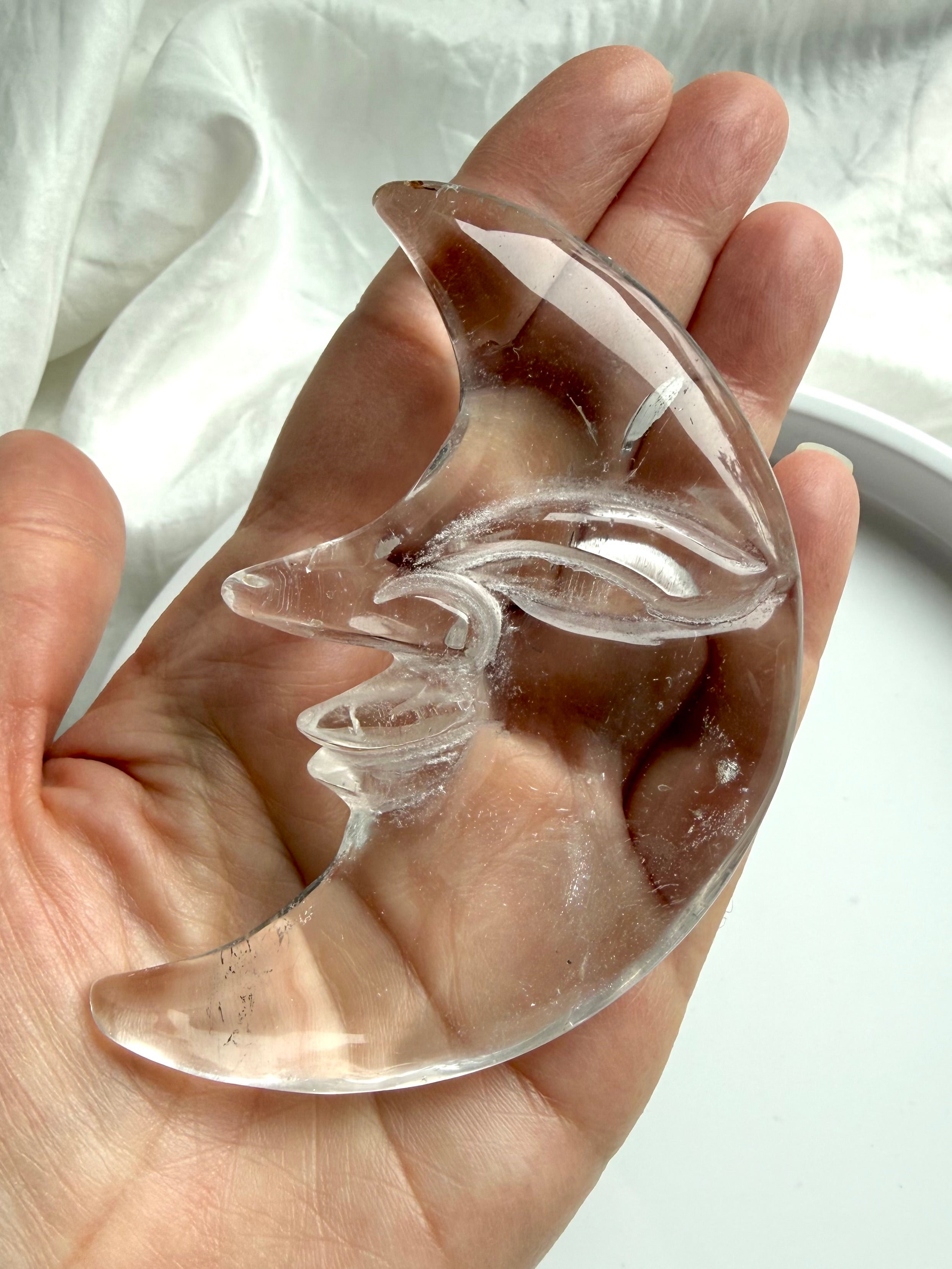 Clear Quartz Moon Face carving resting in hand, showcasing detailed carving on both sides and water-clear crystal clarity