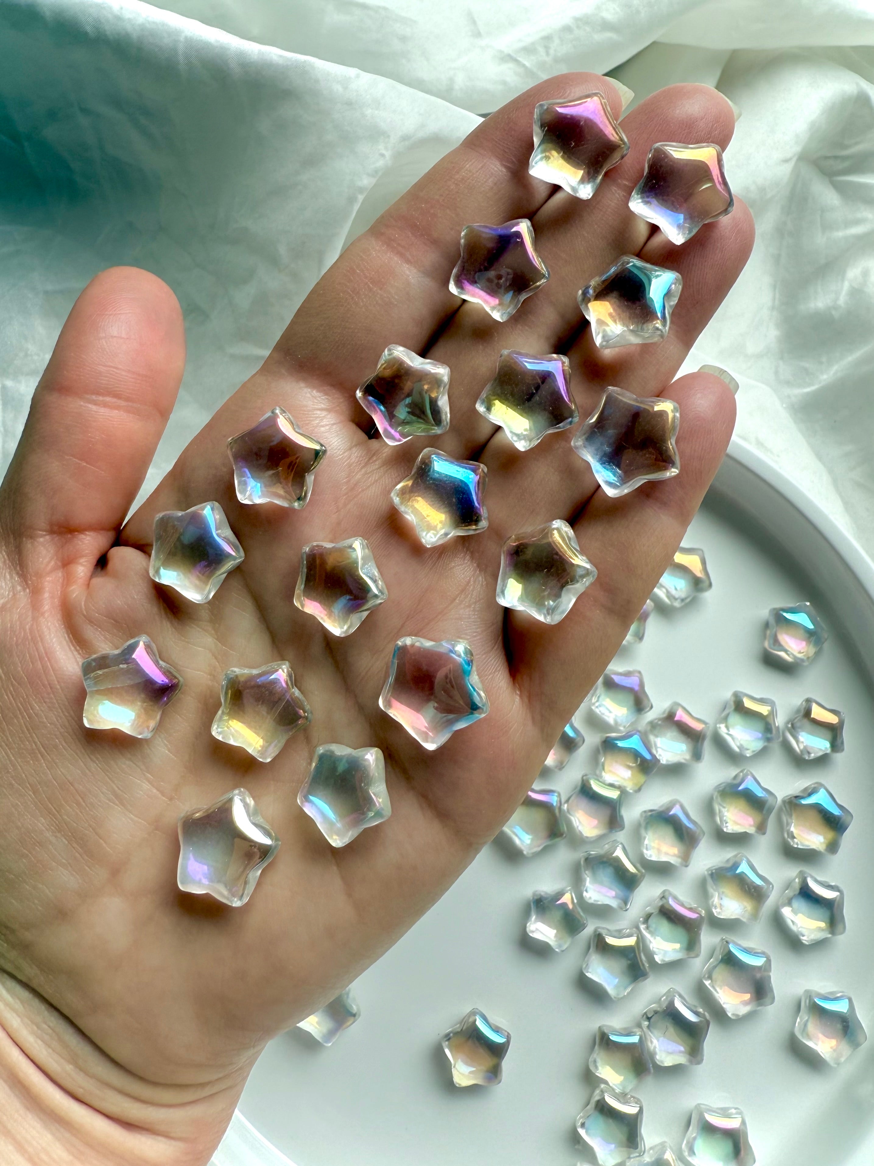 Hand holding mini aura quartz star carvings with opalescent rainbow light — pocket-sized crystals for healing, peace, and meditation